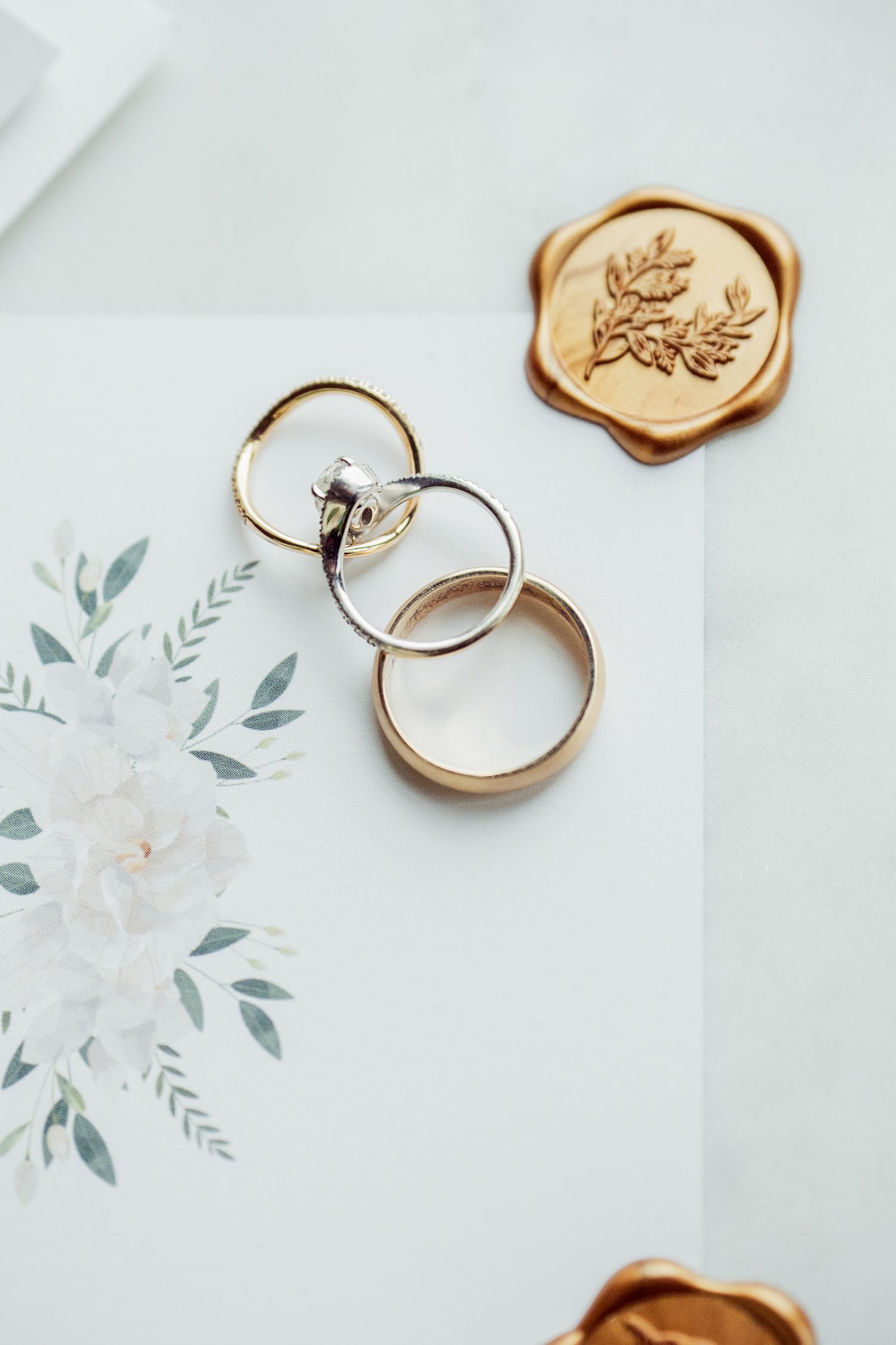 Wedding rings and wax seals arranged with delicate floral watercolor design on light background.