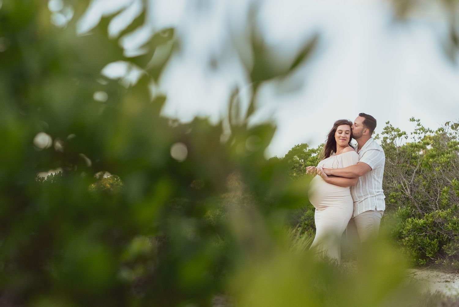 A couple embraces on a beach path surrounded by greenery during a romantic photoshoot.