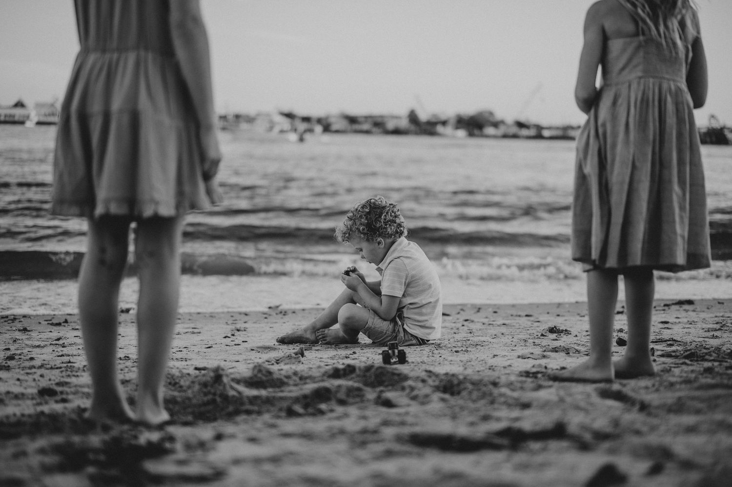 Black and white photo showing people standing together on a beach at sunset.