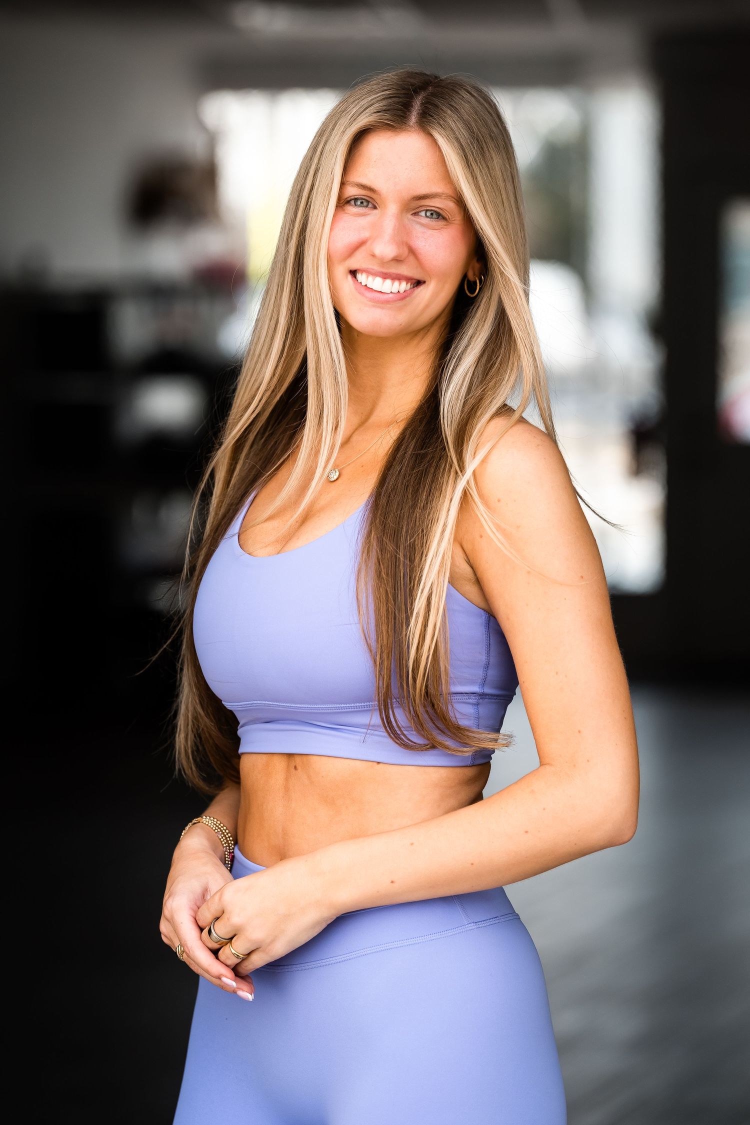 Smiling blonde woman in lavender athletic crop top and leggings set posing confidently in a gym setting.Branding for Rowdy Mermaid