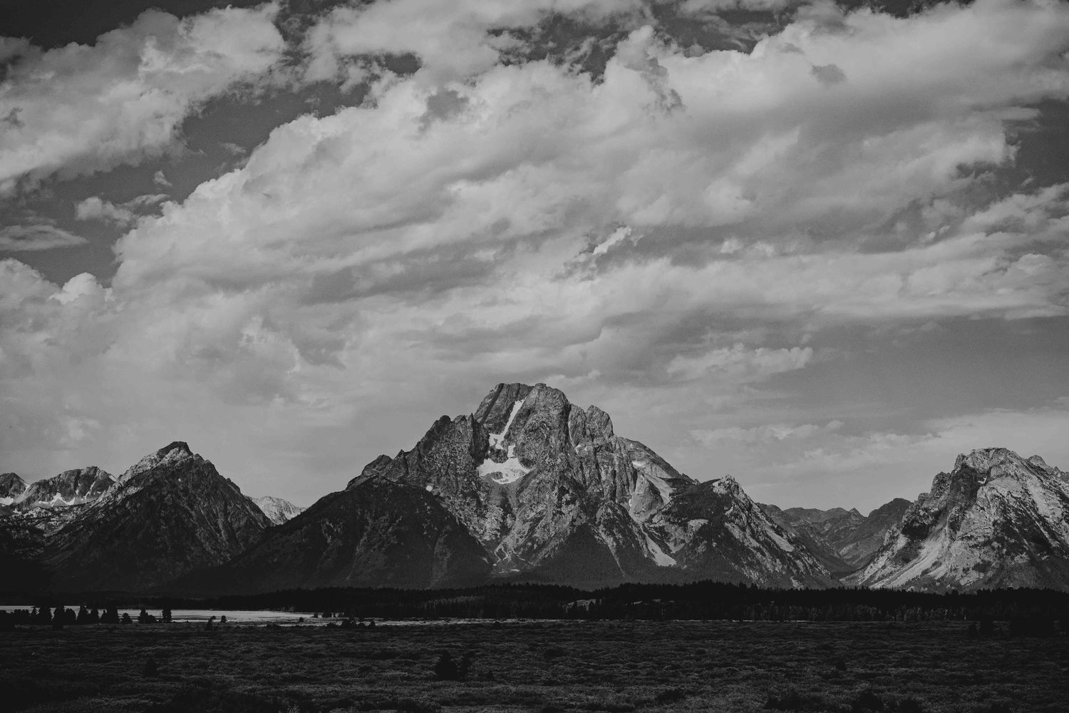 Black and white panoramic view of rugged mountain peaks with dramatic cloud formations.