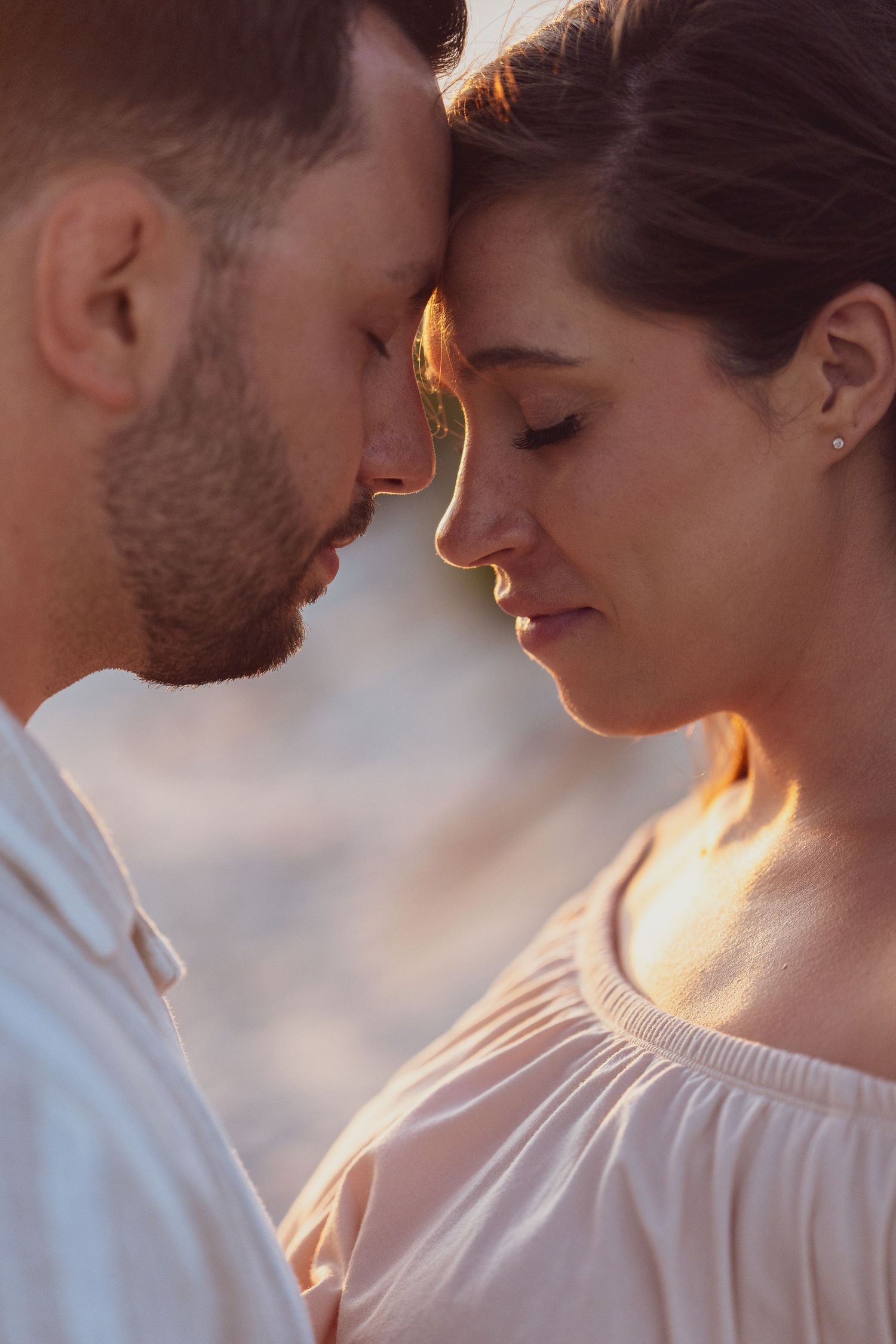 A romantic close-up portrait of a couple touching foreheads in warm sunset light.