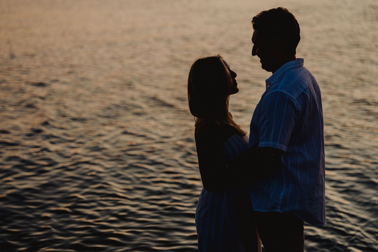 Silhouette of a romantic couple embracing by the water during a golden sunset, creating a dreamy atmosphere.