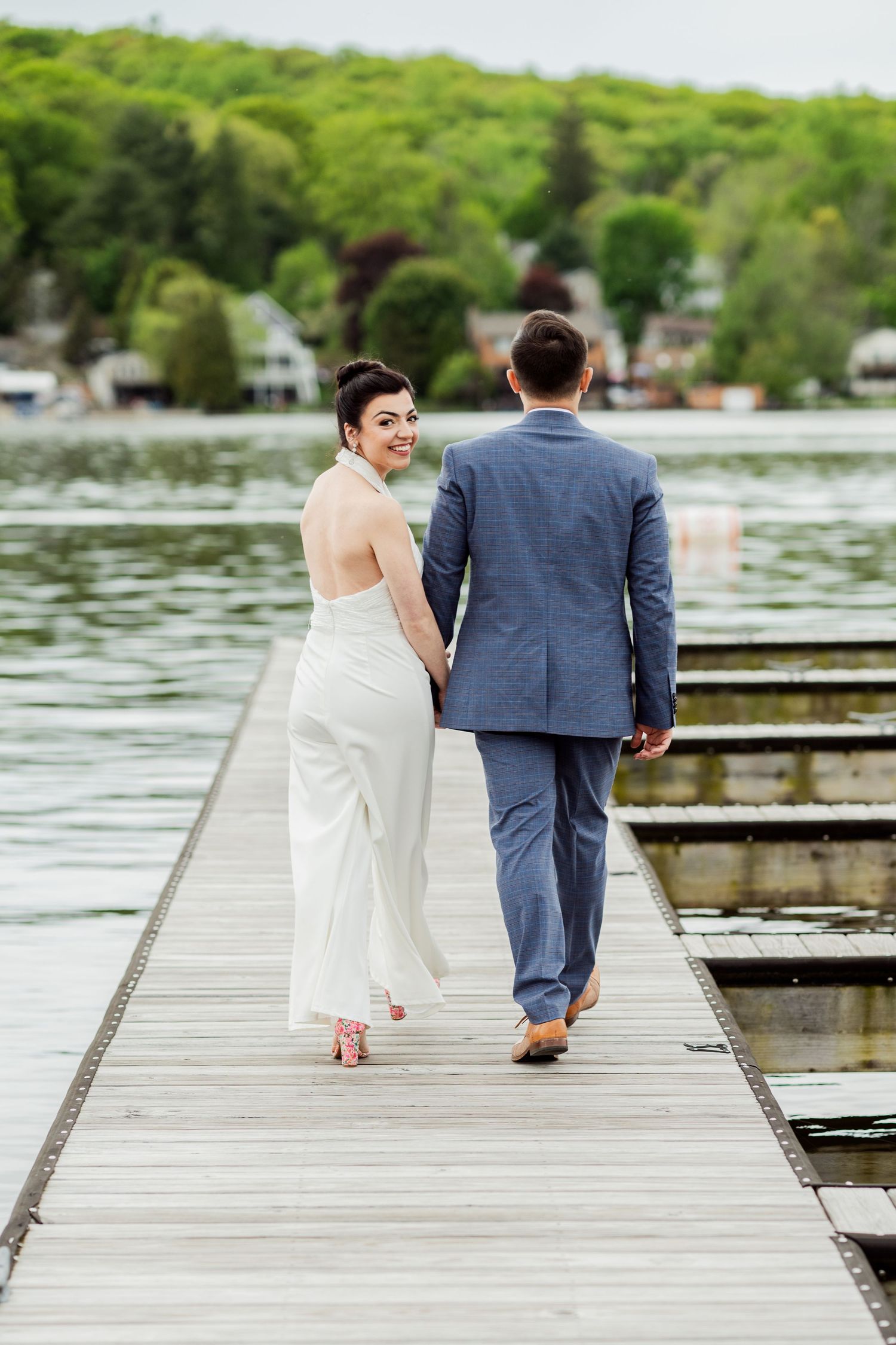 A couple walks together on a wooden dock surrounded by peaceful water and greenery.