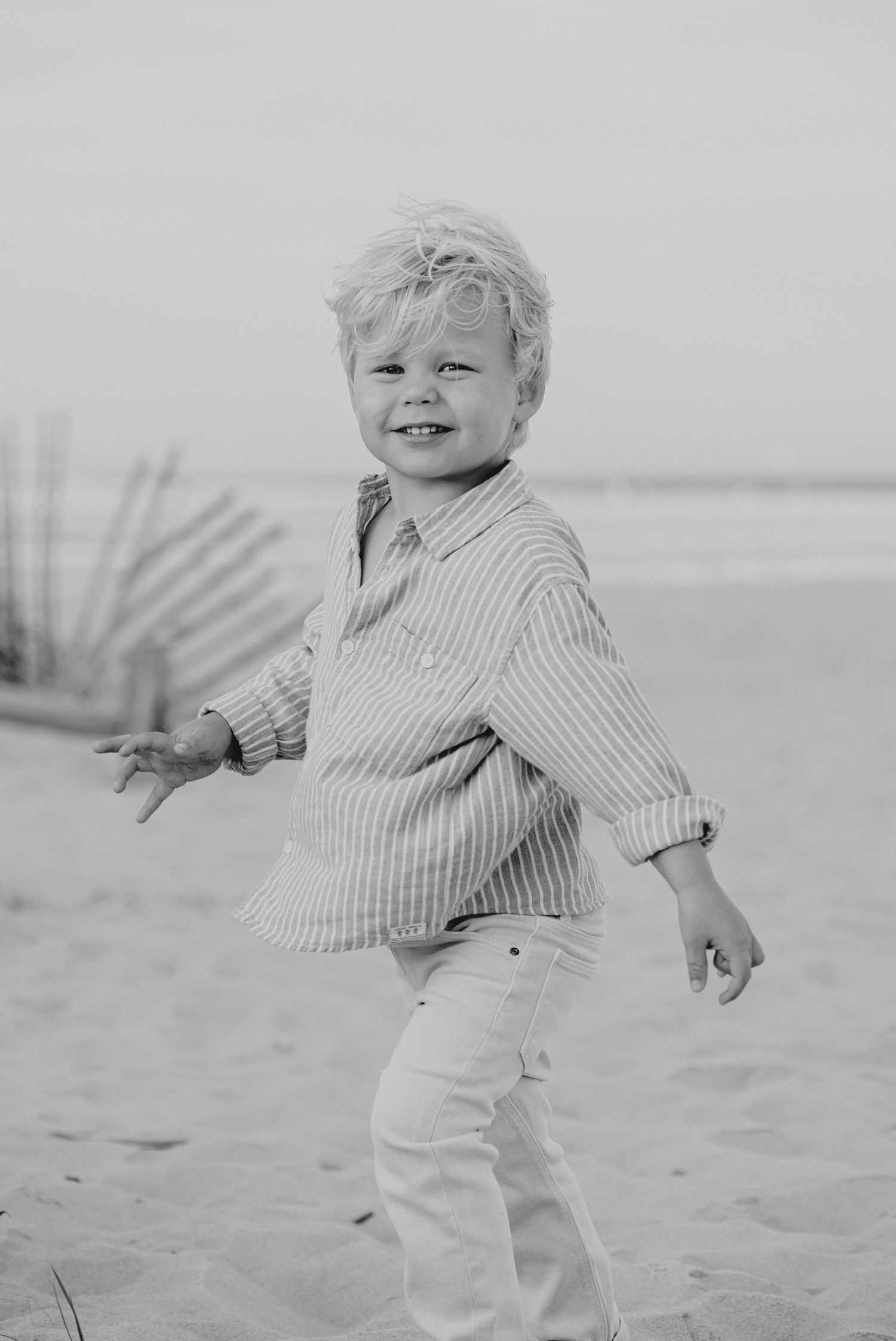 Black and white photo of toddler playing on beach in striped shirt.