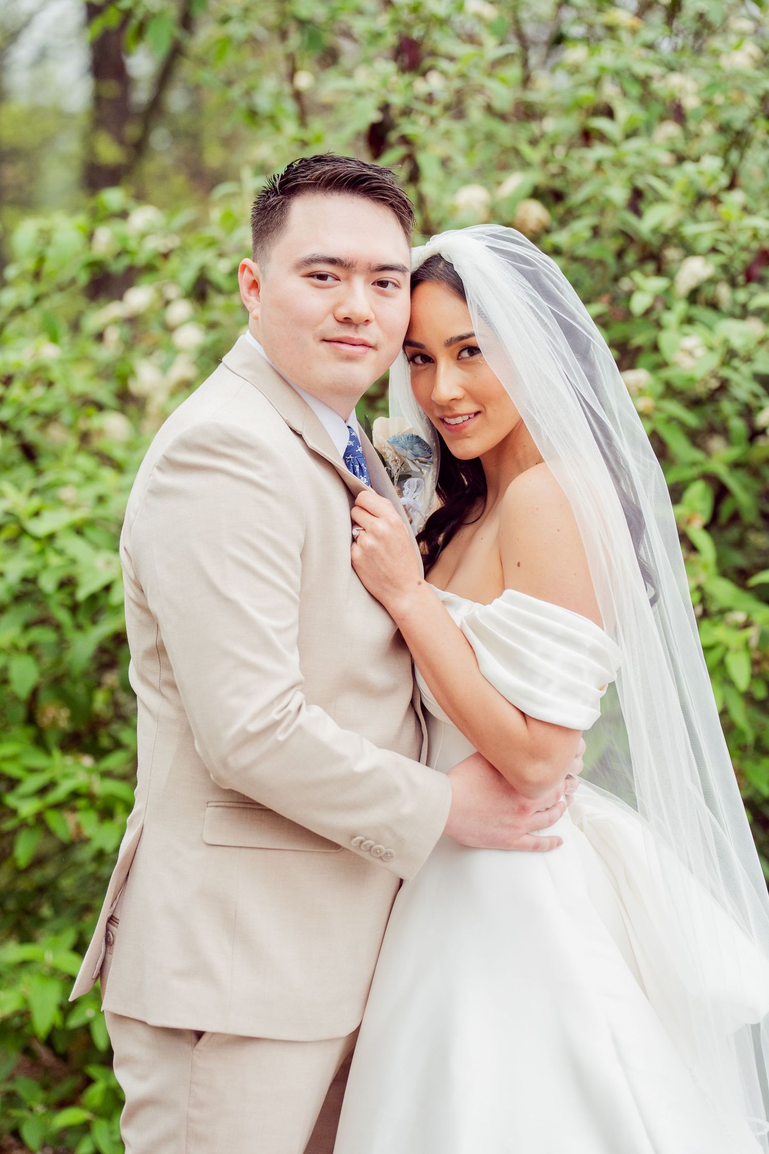 Tender moment between newlyweds in garden setting with natural greenery.