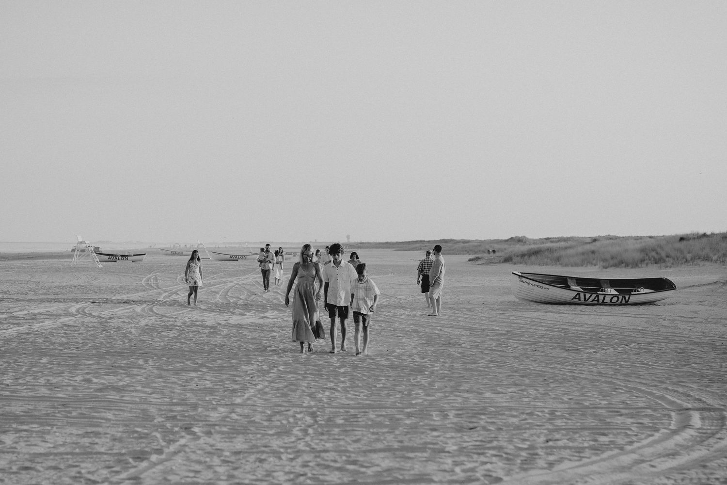 Black and white beach landscape with scattered people and boat silhouettes.