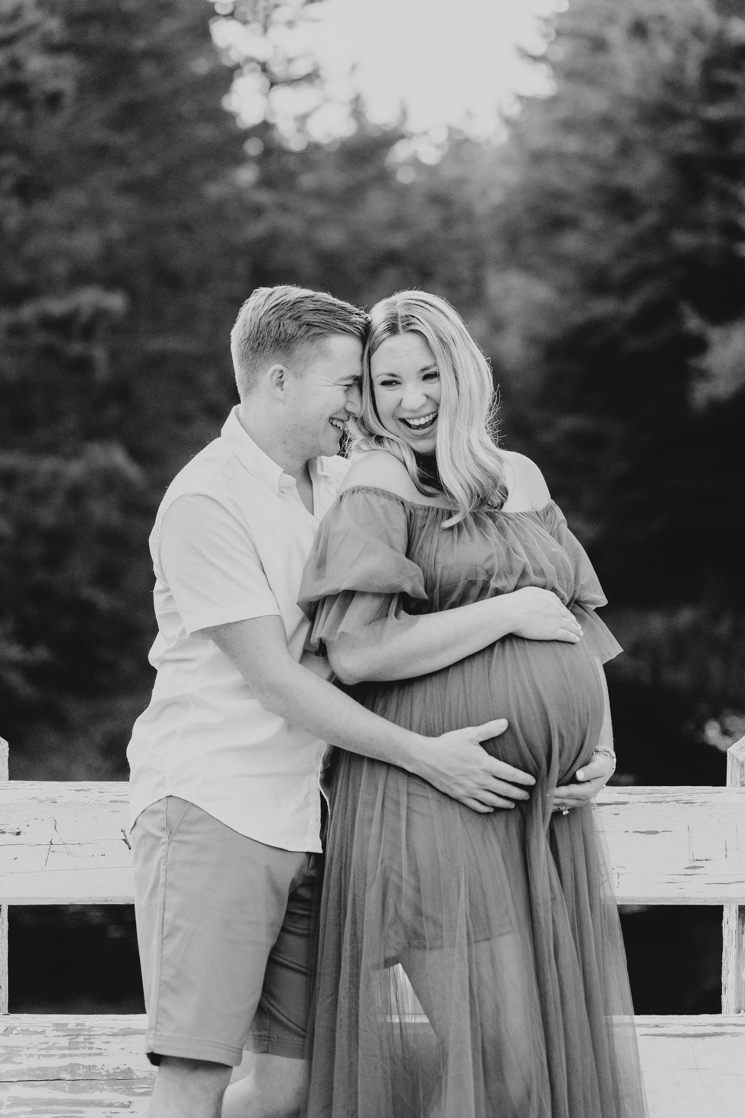 Couple shares intimate moment on white fence during maternity session.