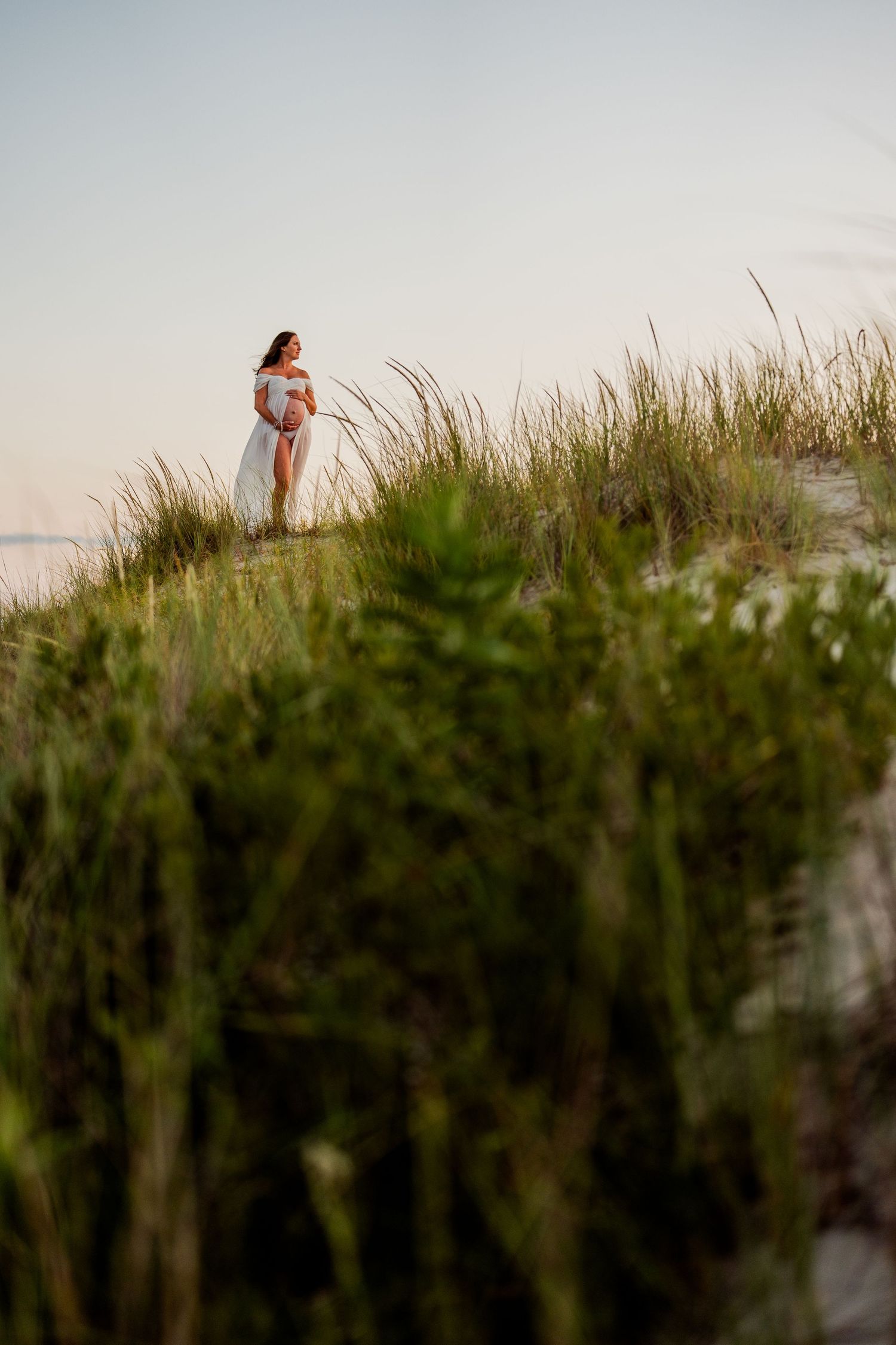Figure stands among tall beach grass during golden hour with ocean in background.
