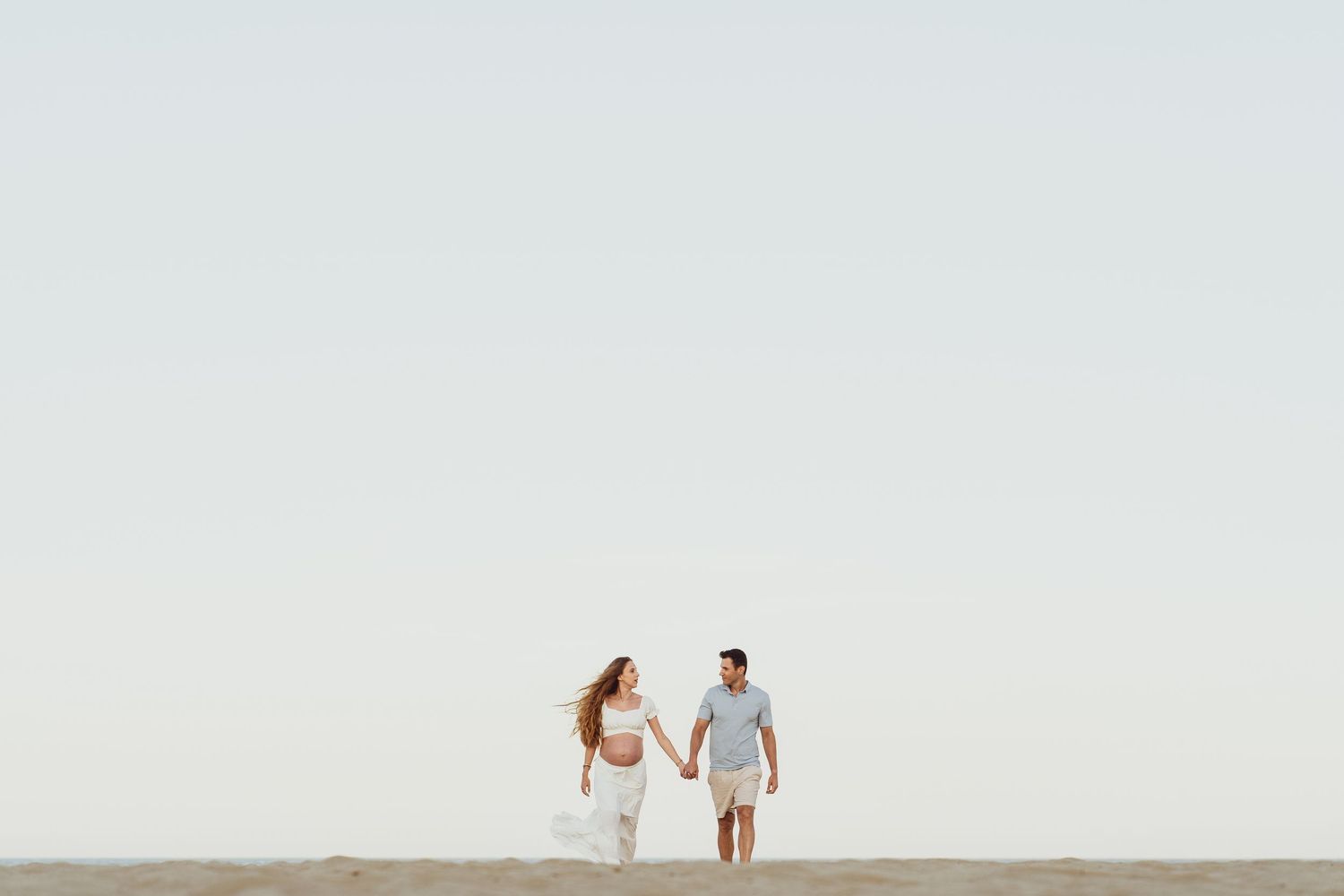 Minimalist beach scene with two figures walking in the distance.