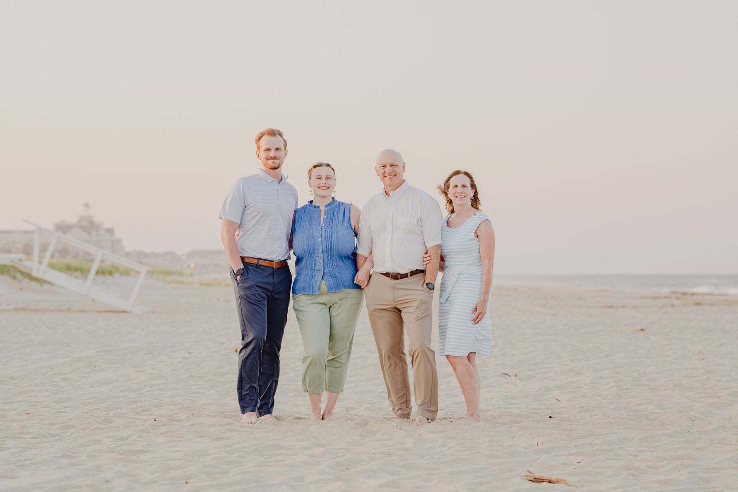 Four adults smiling and posing together on a sandy beach during golden hour in casual summer attire.