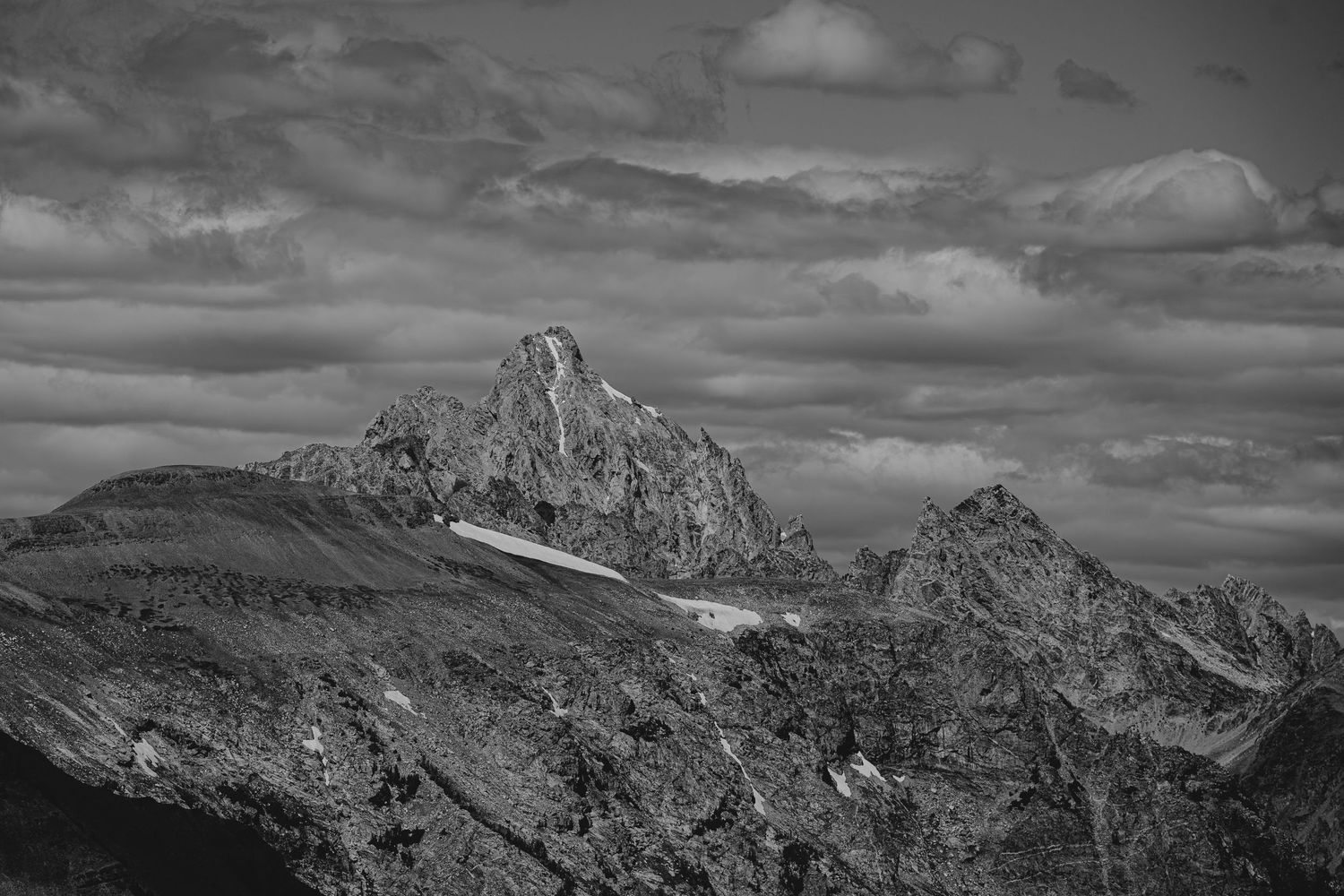 Dramatic black and white panorama of rugged mountain peaks with moody clouds in the sky.