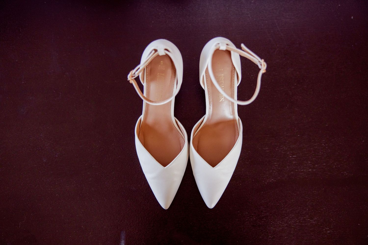Elegant white bridal shoes arranged on dark background for wedding day photography.