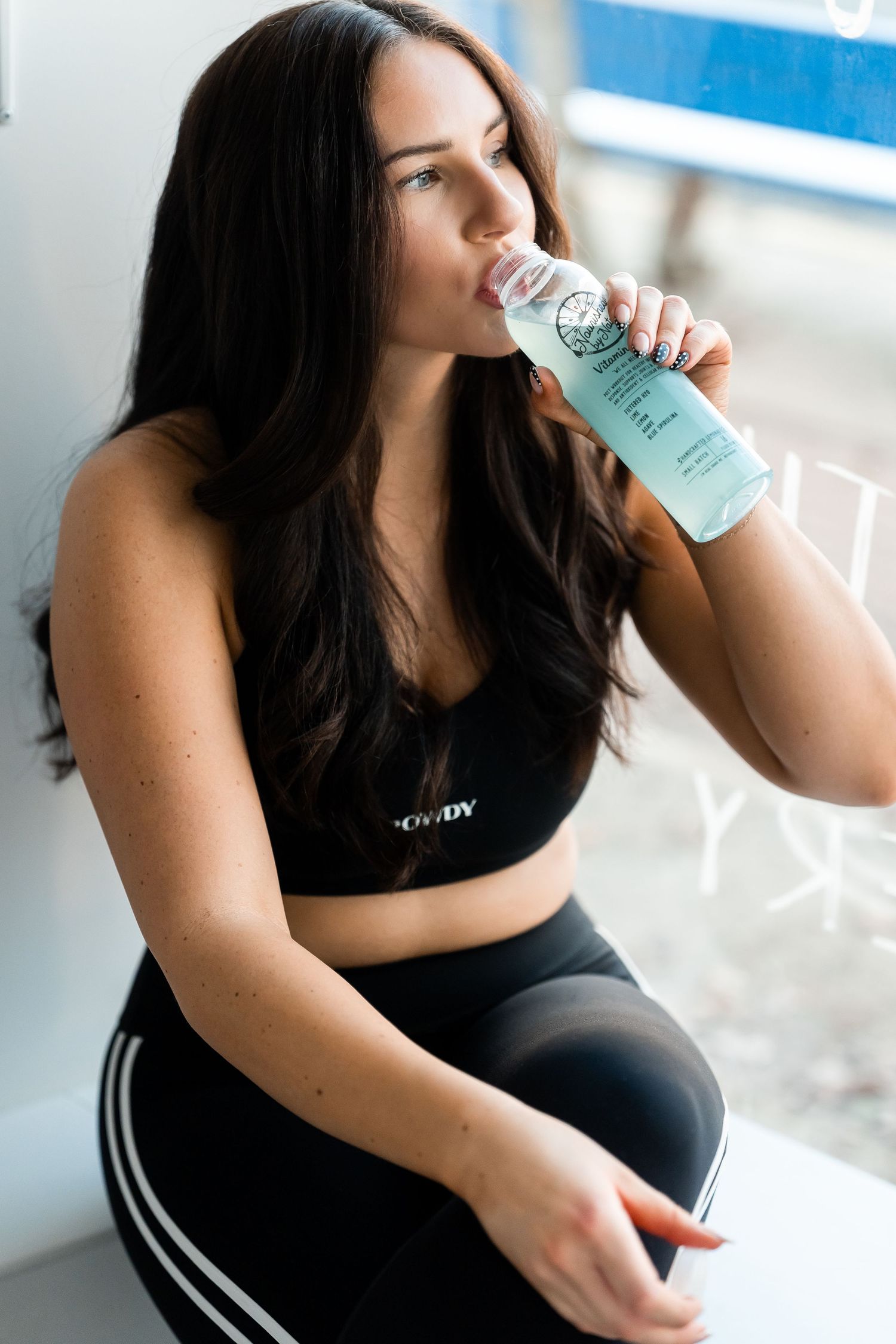 Athletic woman in black workout attire drinks from a water bottle during fitness session.
