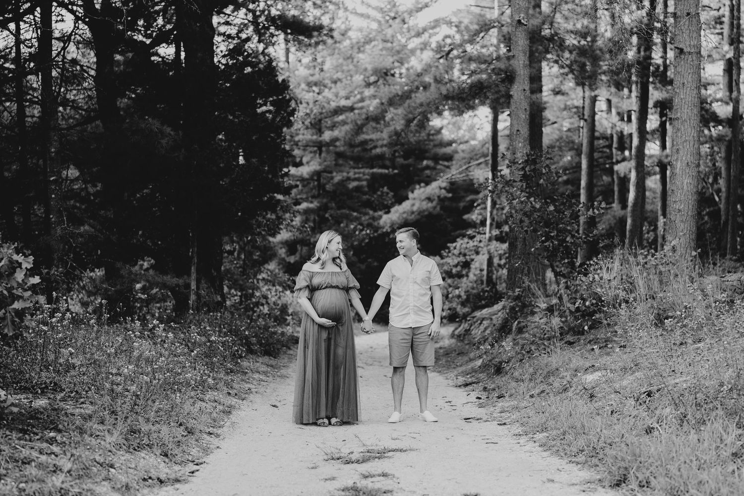 Black and white photo of a couple walking hand in hand down a wooded path.