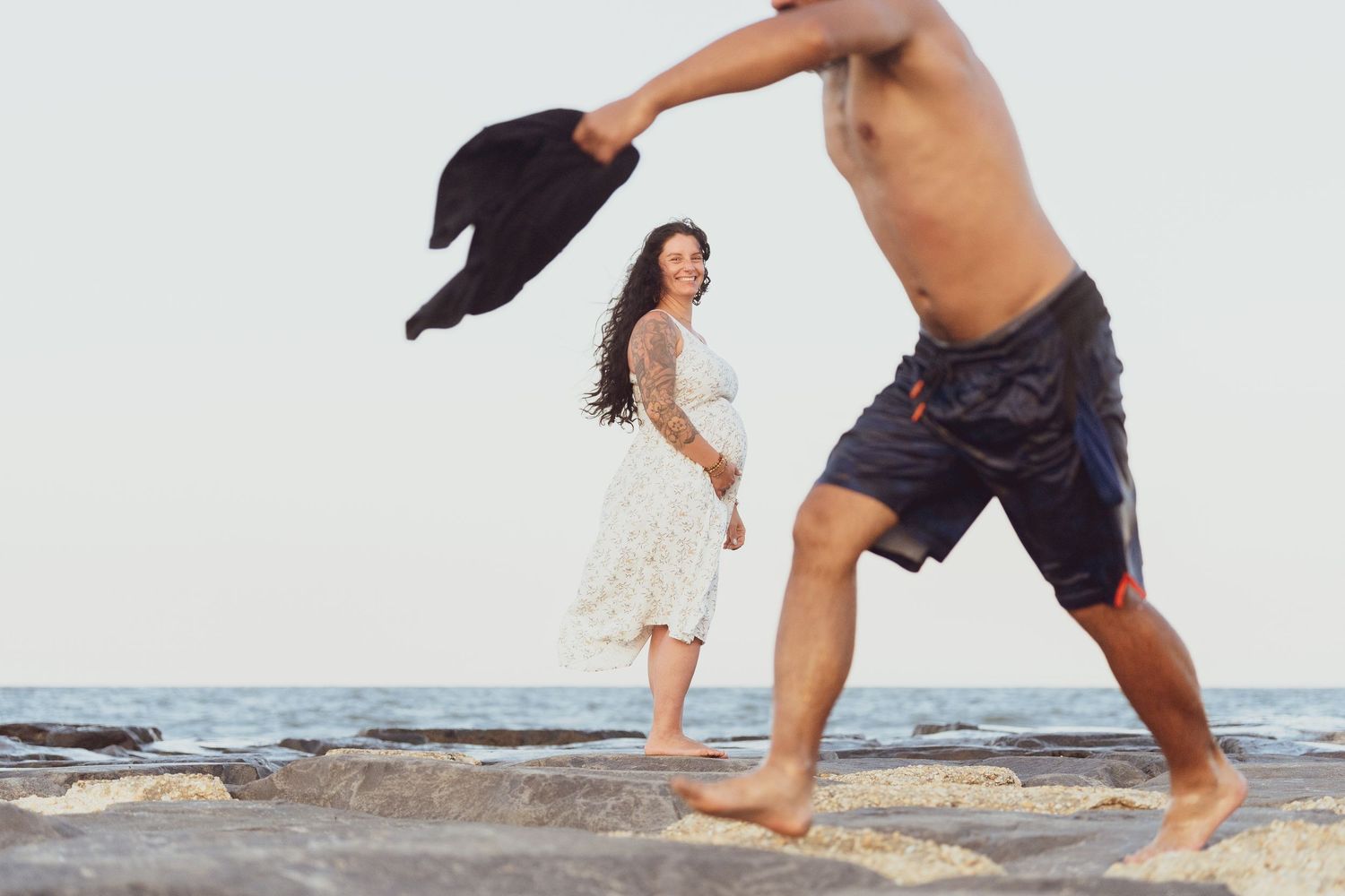 Playful beach photoshoot with people running and holding a hat by the ocean.