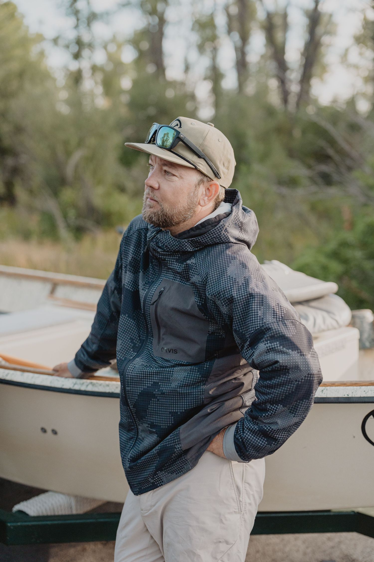 Person in a navy blue rain jacket and baseball cap stands beside a boat in an outdoor setting.