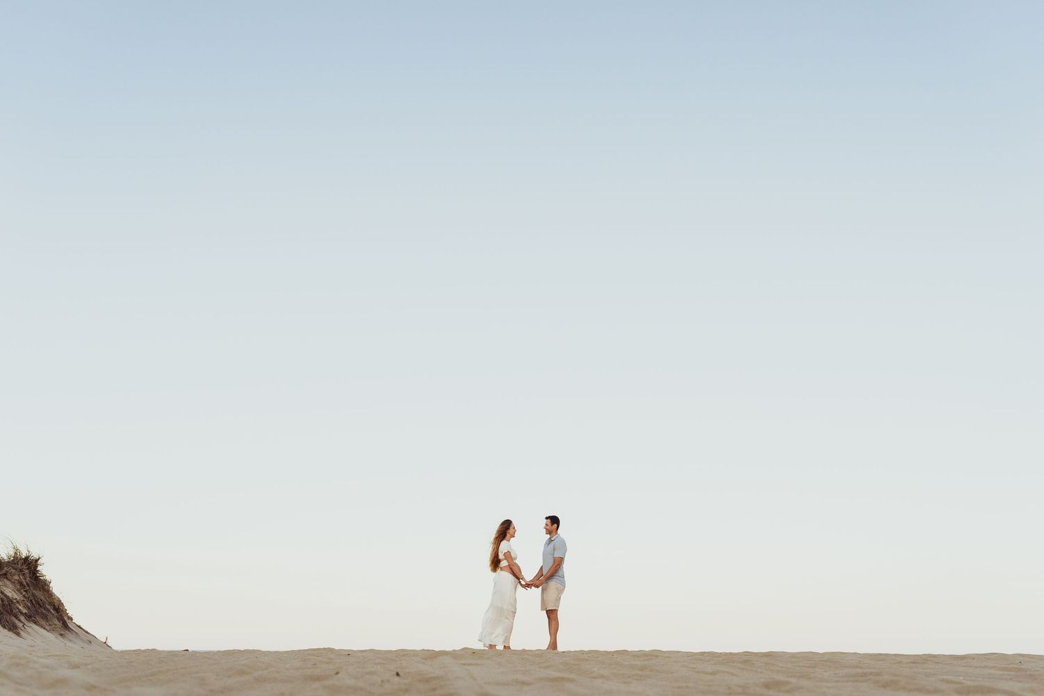 A couple shares a romantic moment while standing on a sandy beach during sunset.