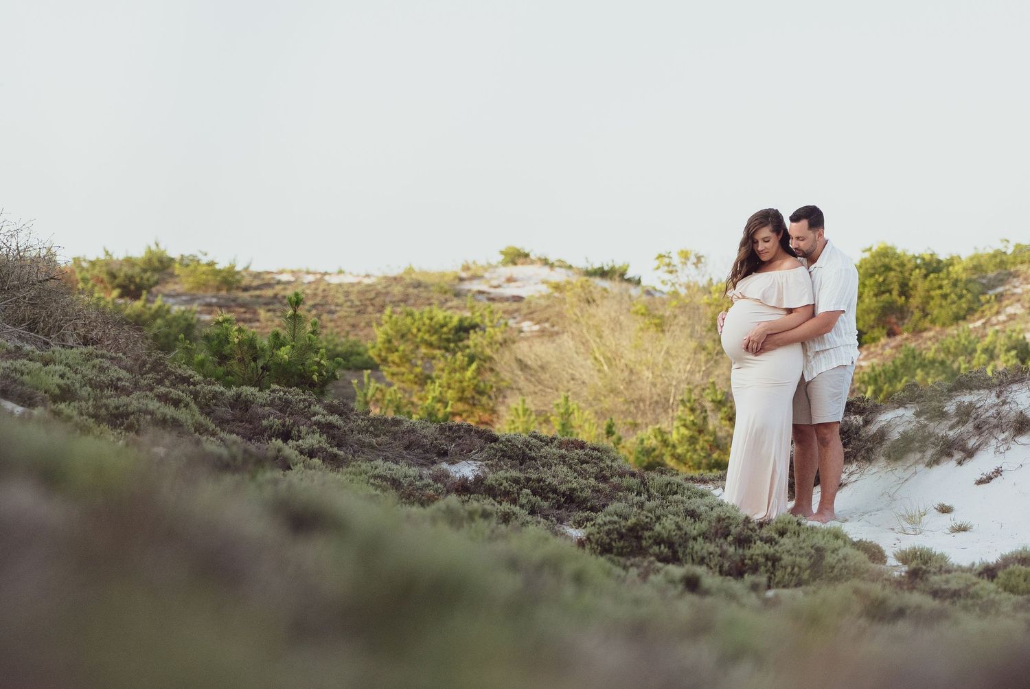 Couple standing together on coastal dunes during golden hour.