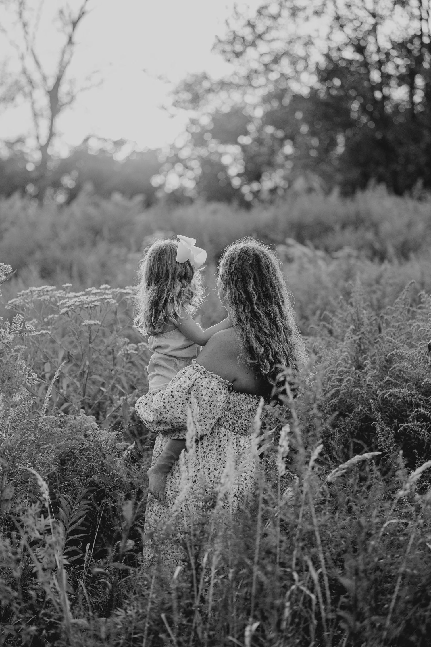Black and white portrait of two figures embracing in a wildflower meadow.
