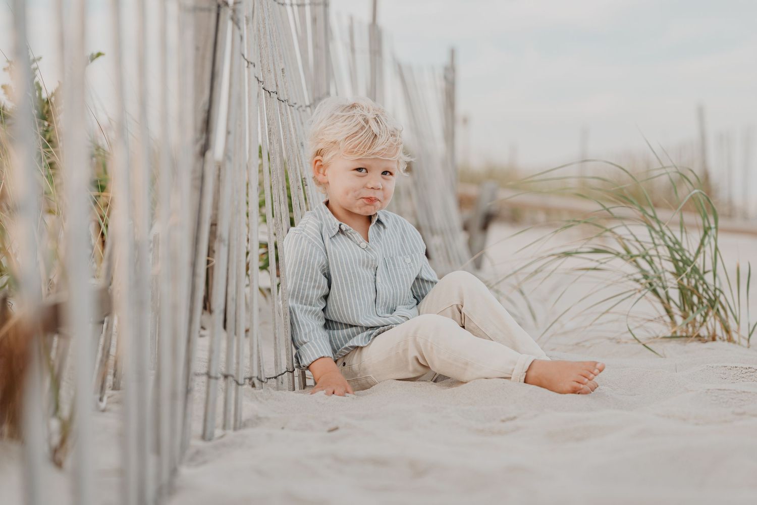 Child resting on wooden beach fence surrounded by sea grass.
