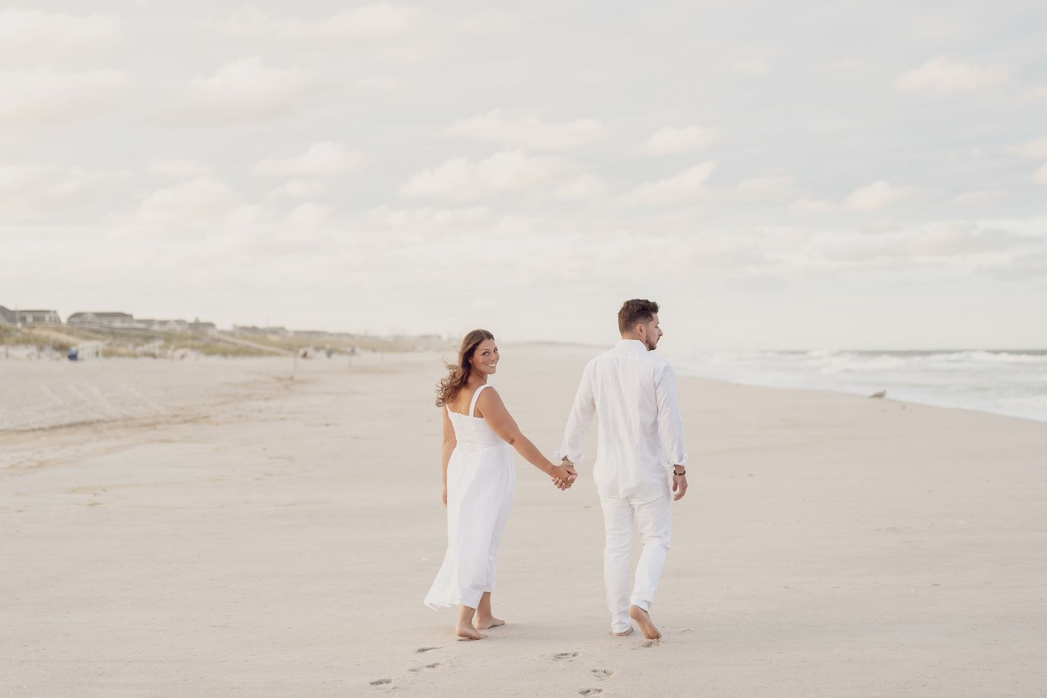 People in white clothing walking along serene beach shoreline at sunset.