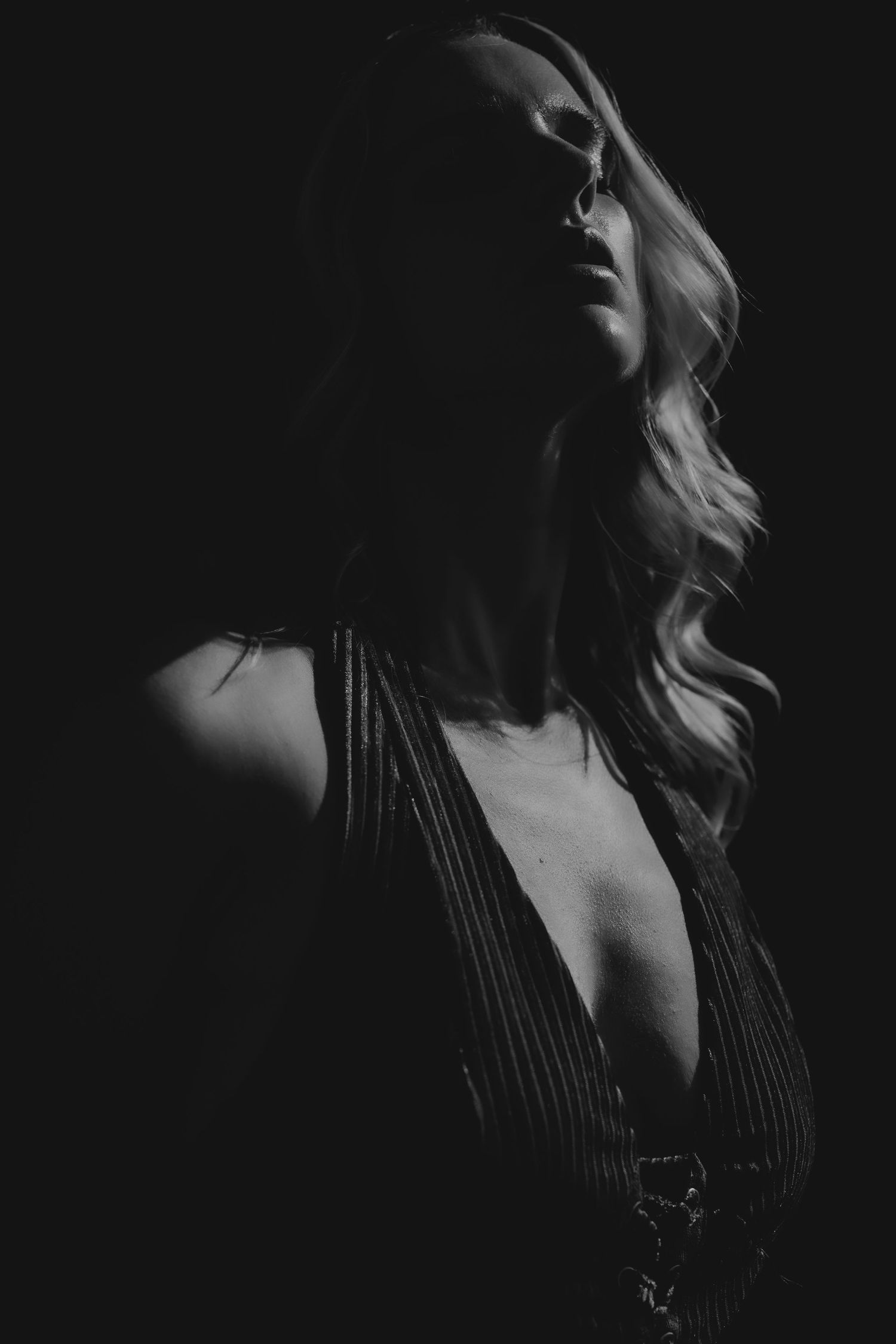 Black and white portrait of a woman with wavy hair in dramatic low-key lighting wearing a deep V-neck top.
