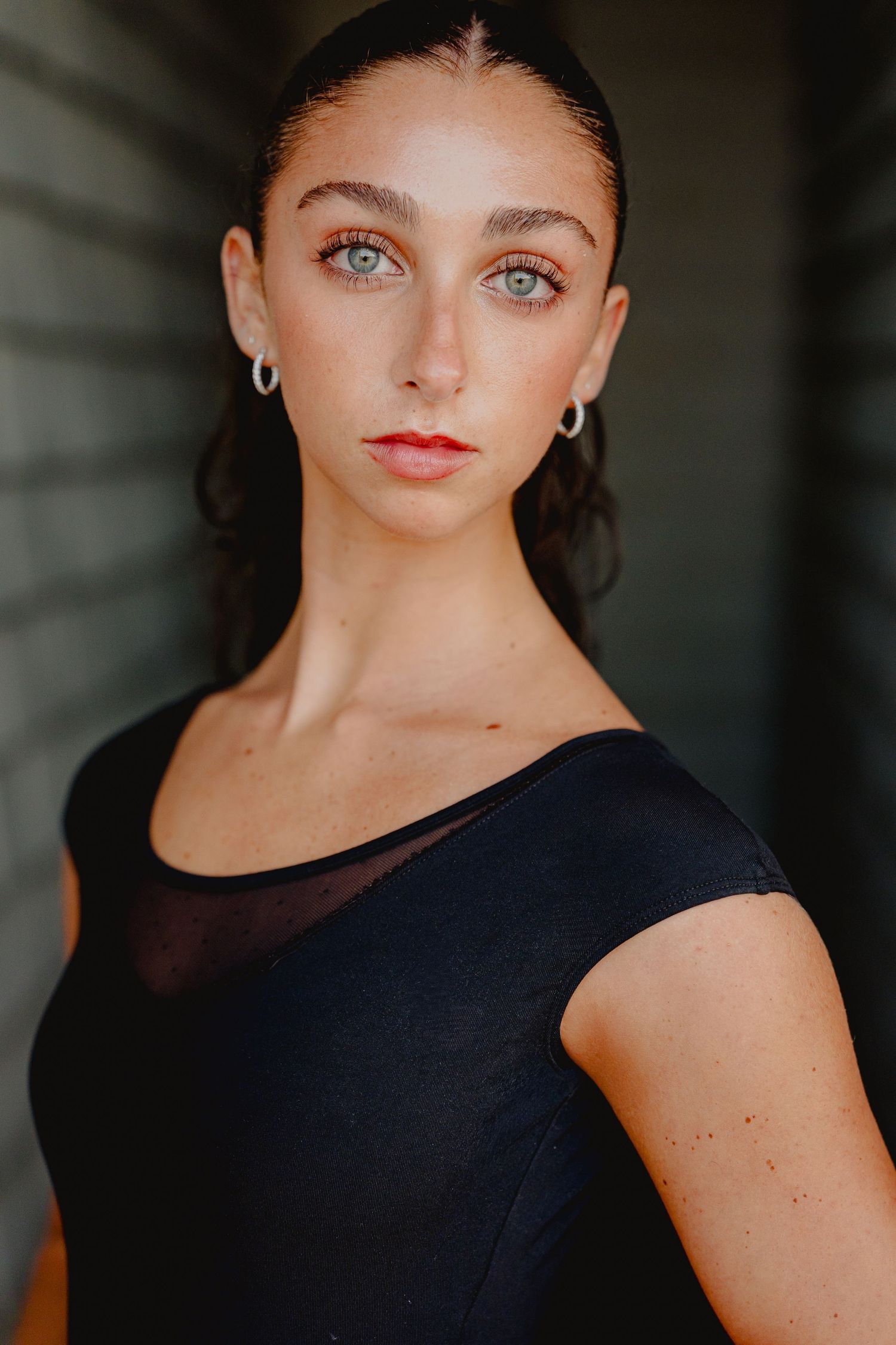 Young woman with green eyes wearing silver hoop earrings and black top poses for portrait photo.