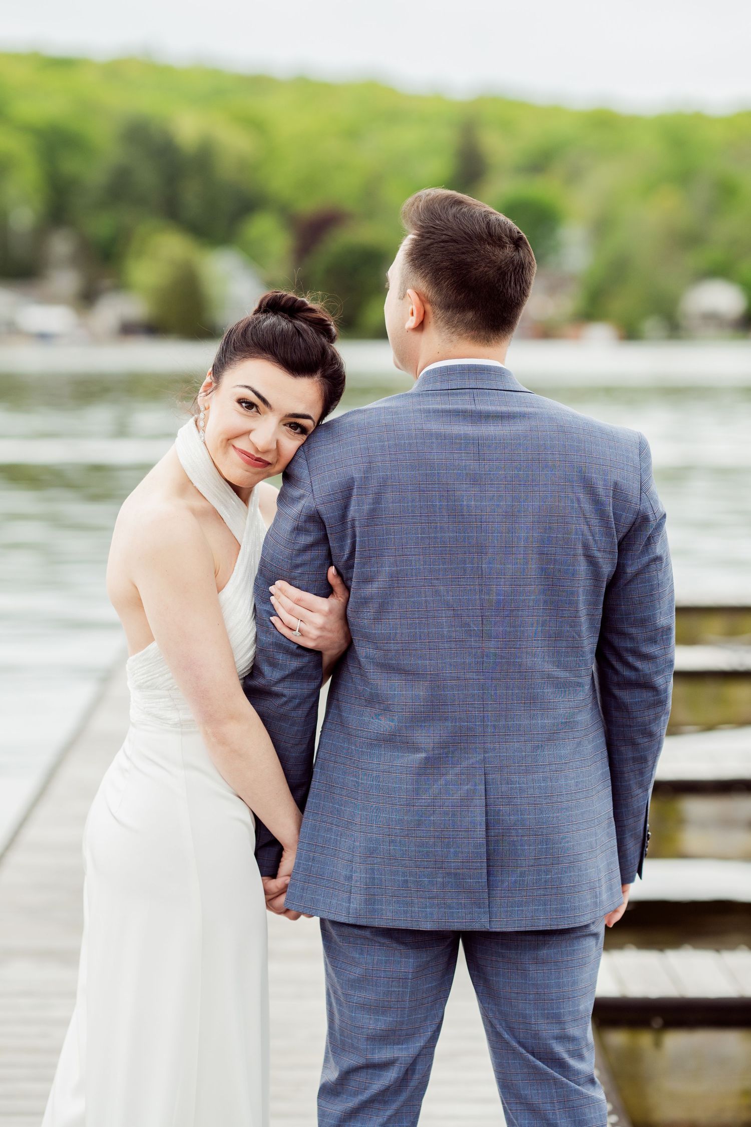 A couple in wedding attire shares playful moments on a dock overlooking a lake.