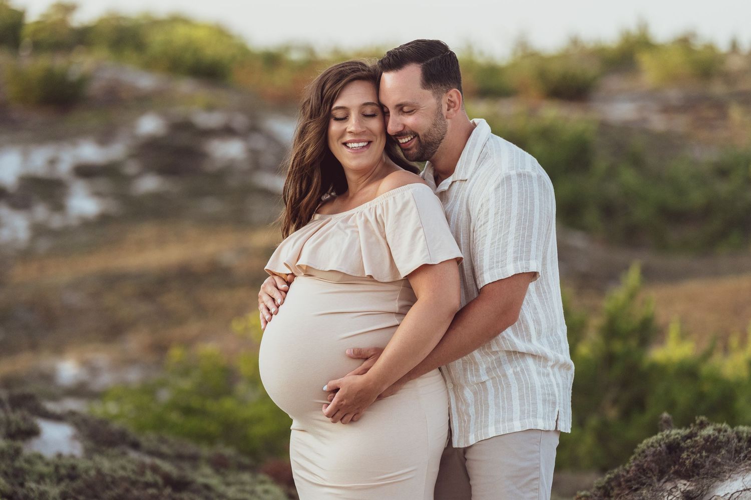 Intimate maternity photo of couple embracing outdoors in natural setting at sunset.