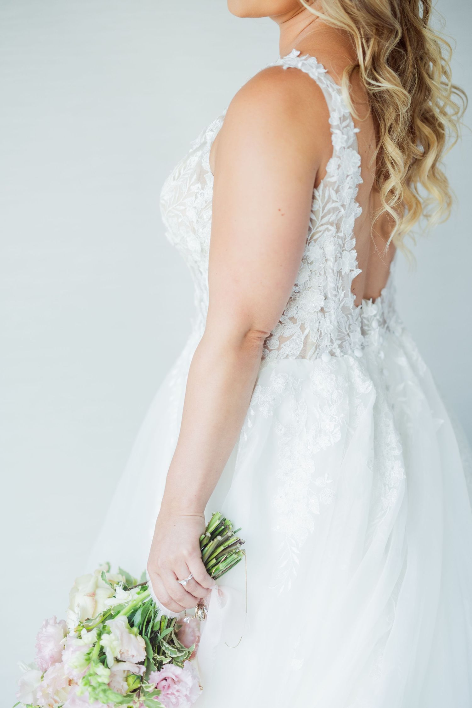 Side view of flowing white wedding dress with lace details and floral bouquet.