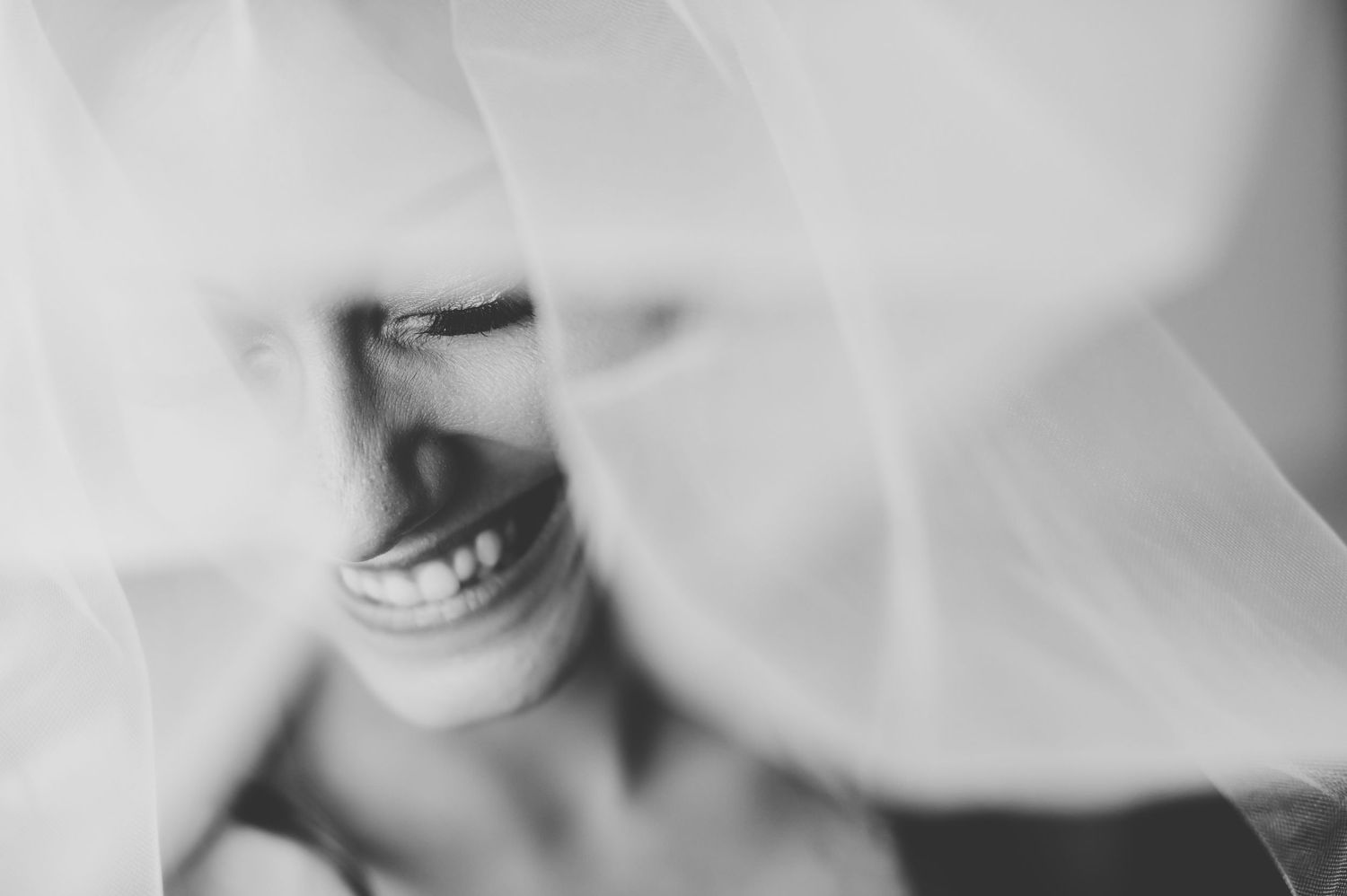 Black and white photo of a smiling bride partially covered by a flowing wedding veil.