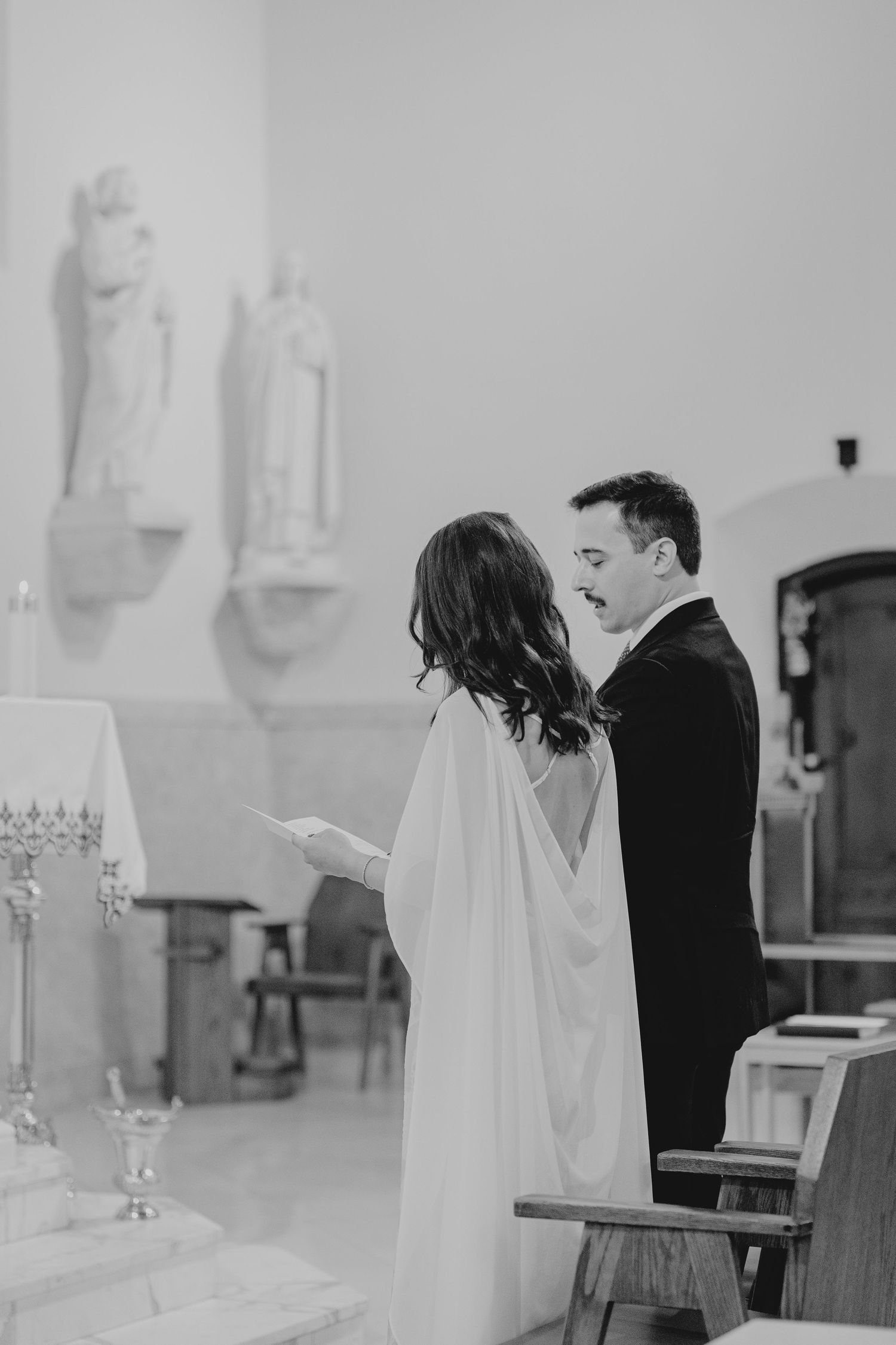 Black and white photo of bride and groom exchanging vows at the altar of a Catholic church.