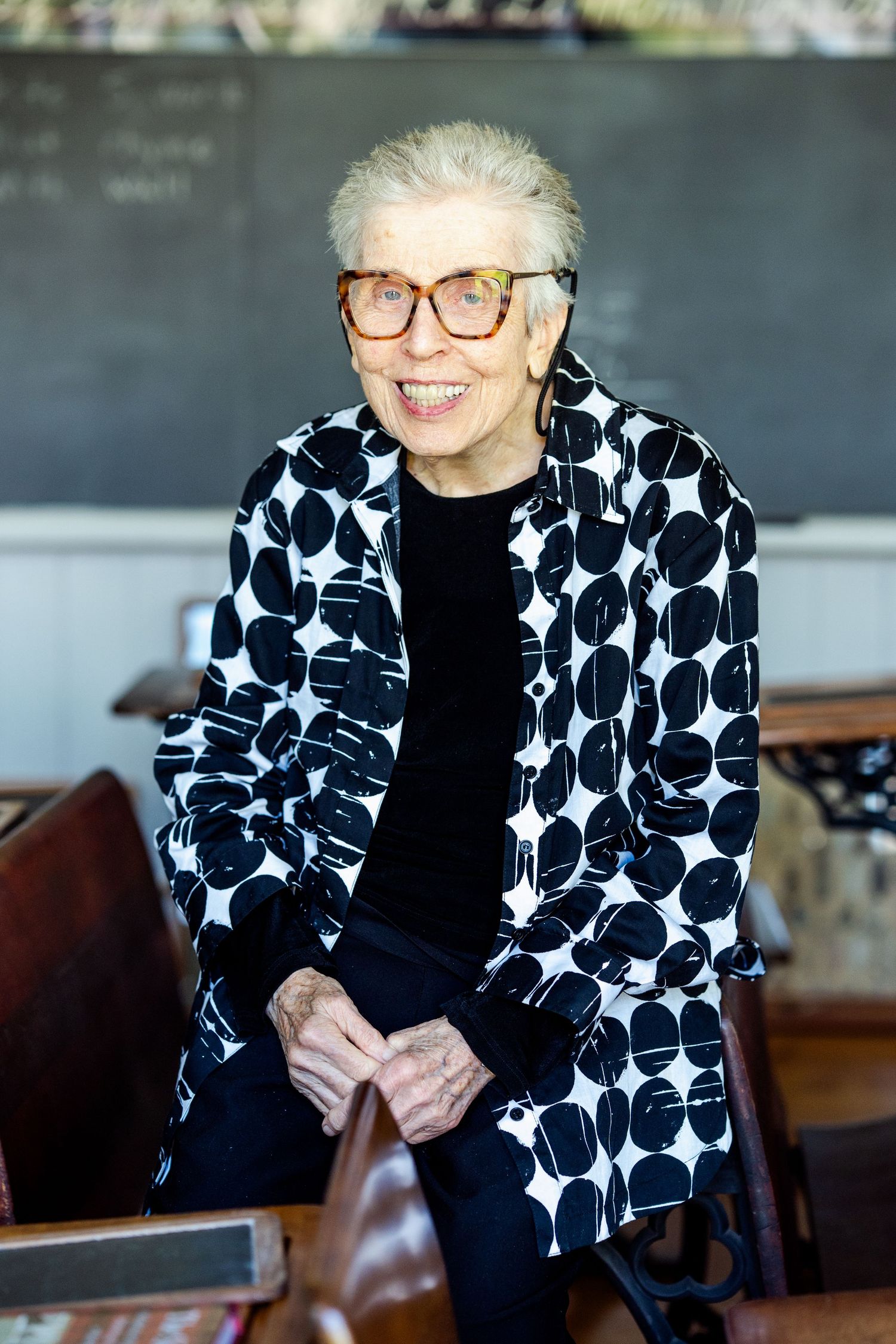 Person wearing black and white polka dot blazer and glasses sits at table with warm lighting.