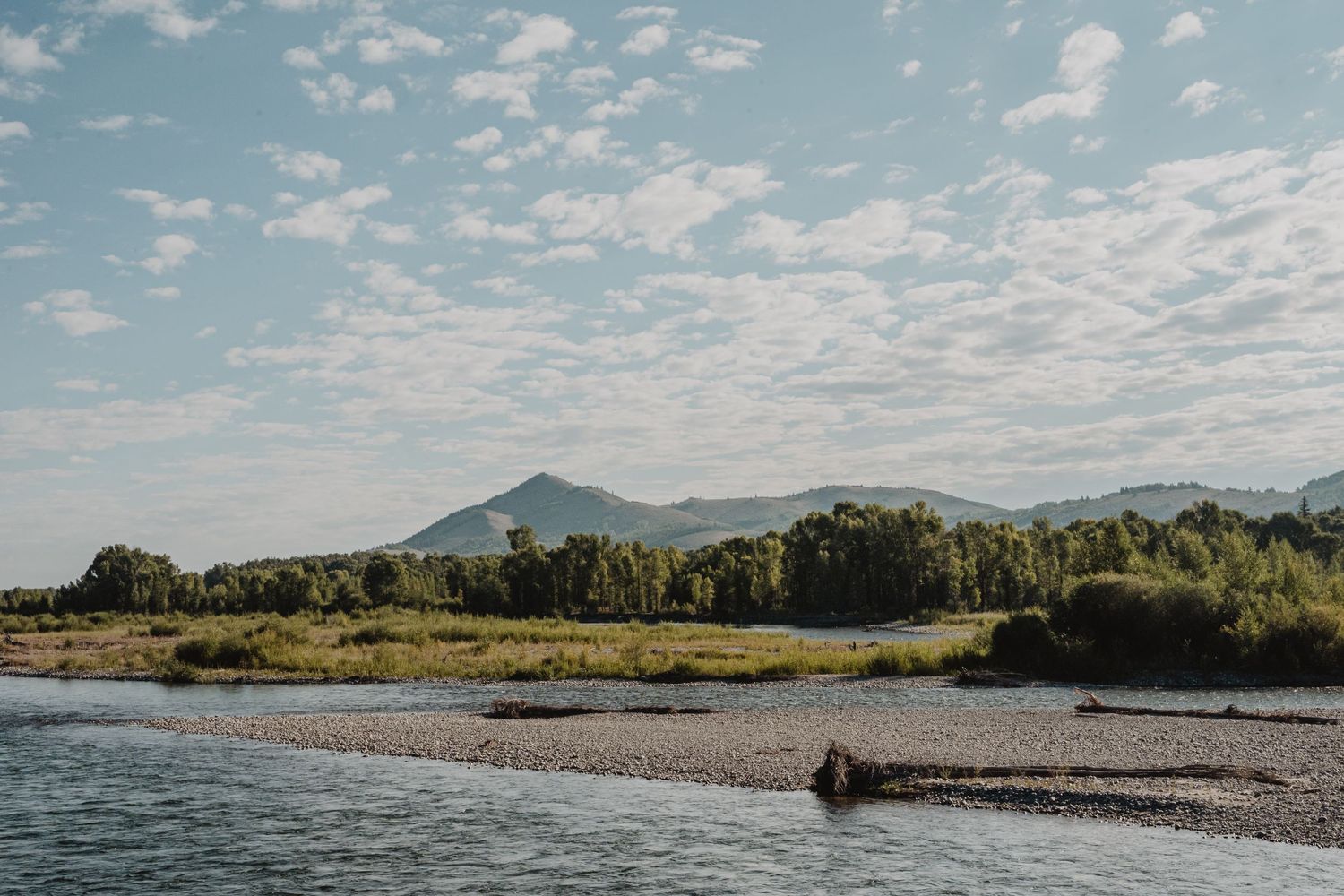 Scenic lakeside view with mountains, trees, and blue skies reflecting on calm waters.