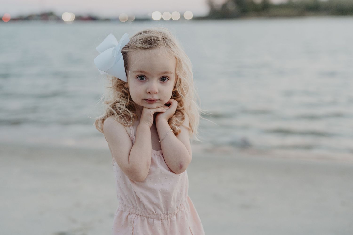 Soft portrait taken at sunset on a beach with bokeh lights in the background.