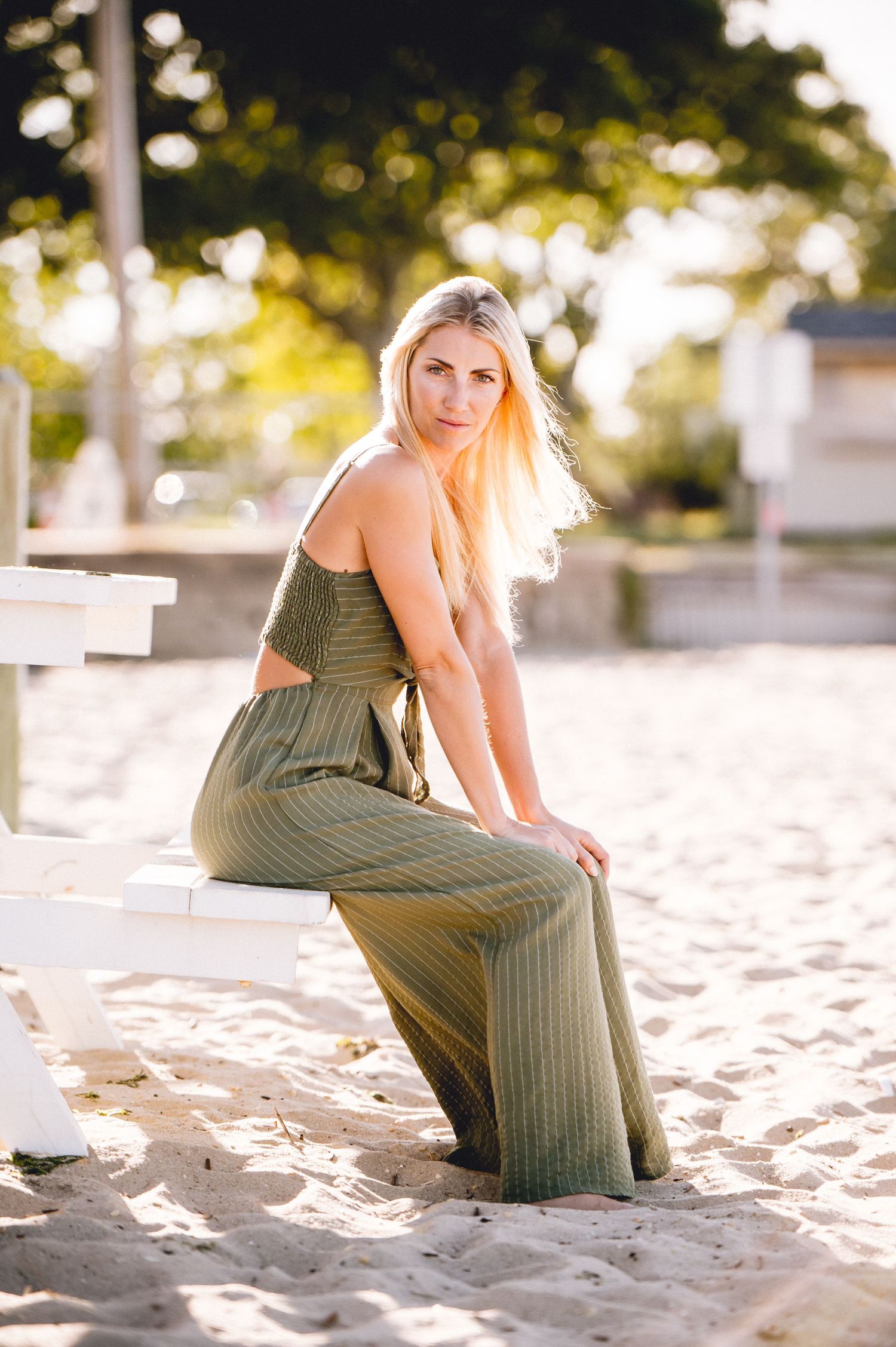 A person in an olive green dress poses on a sandy beach during golden hour in a series of artistic photos.