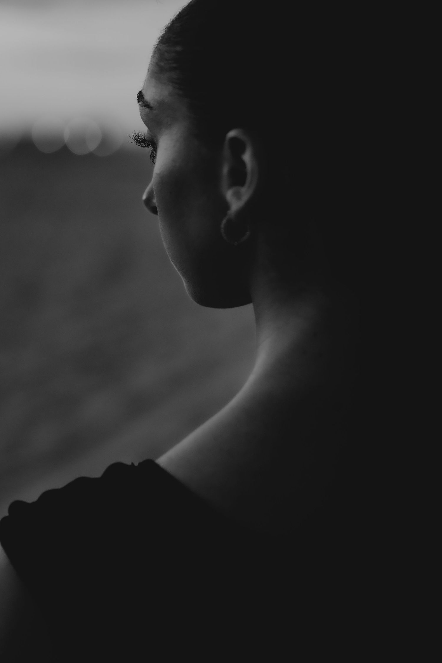 Black and white portrait of a young woman in profile, with soft bokeh background lighting.