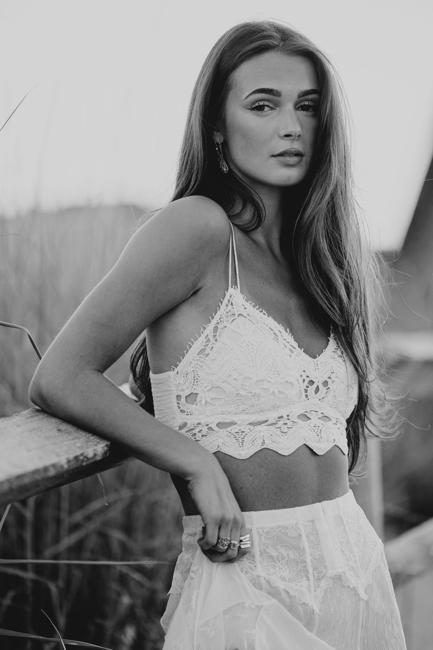 Black and white photo of a young woman in a white lace bralette and sheer skirt posing outdoors.