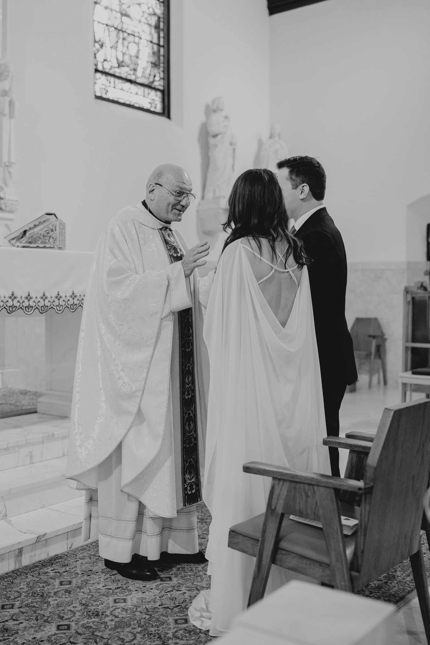 Priest greeting bride and groom at church altar during wedding ceremony in black and white photo.
