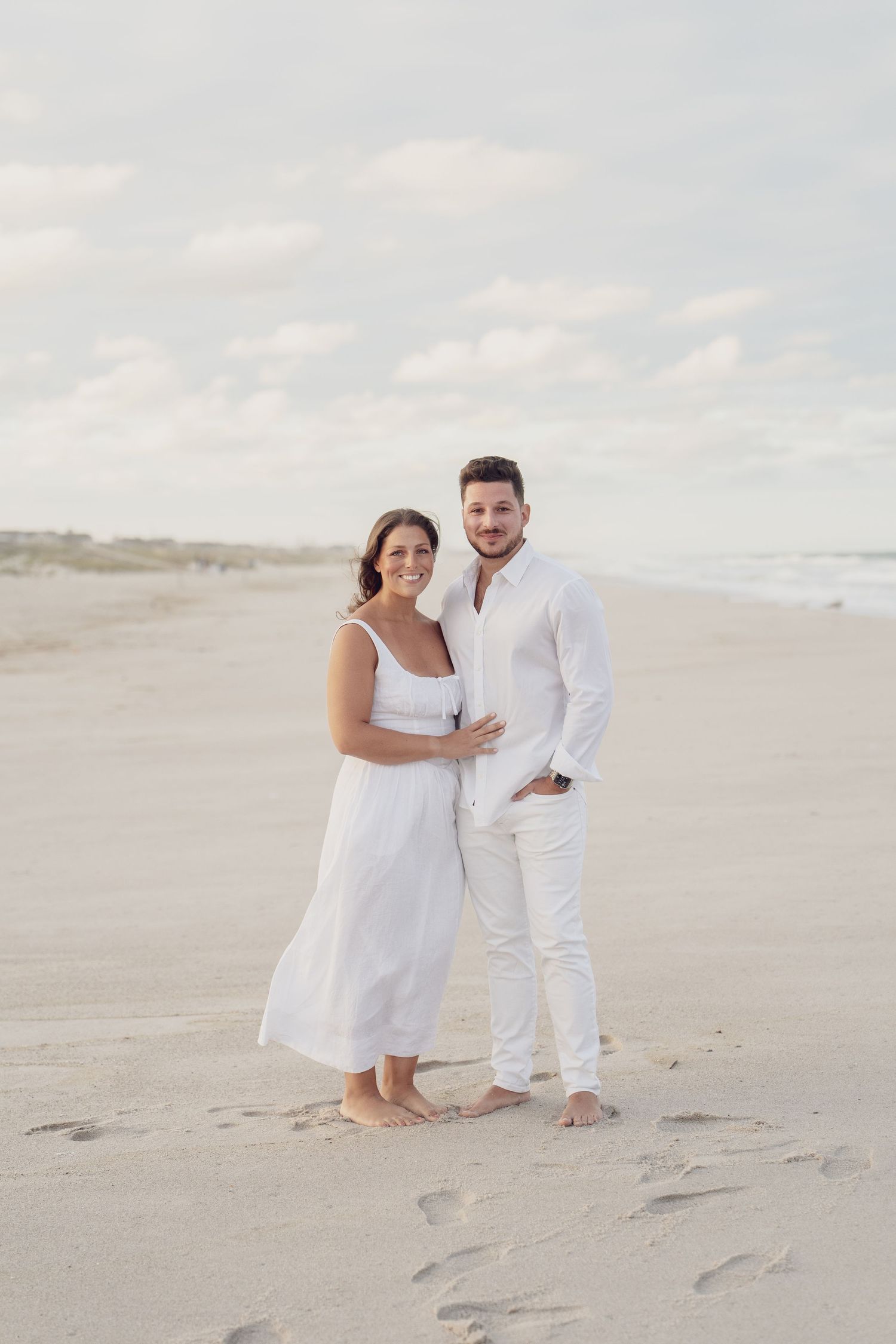 Couple in matching white outfits sharing joyful moments on pristine beach.