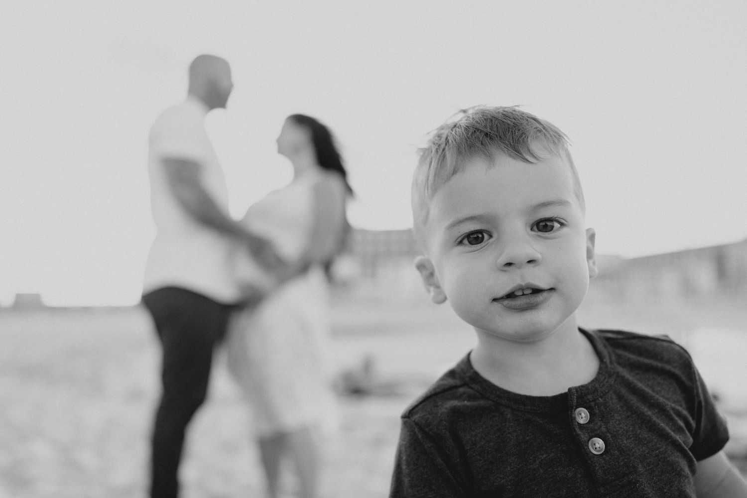 A child smiles at the camera while family members interact in the background.