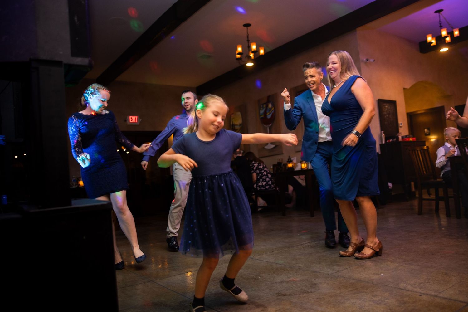 Wedding guests dance energetically on the dance floor during a reception celebration with blue lighting.