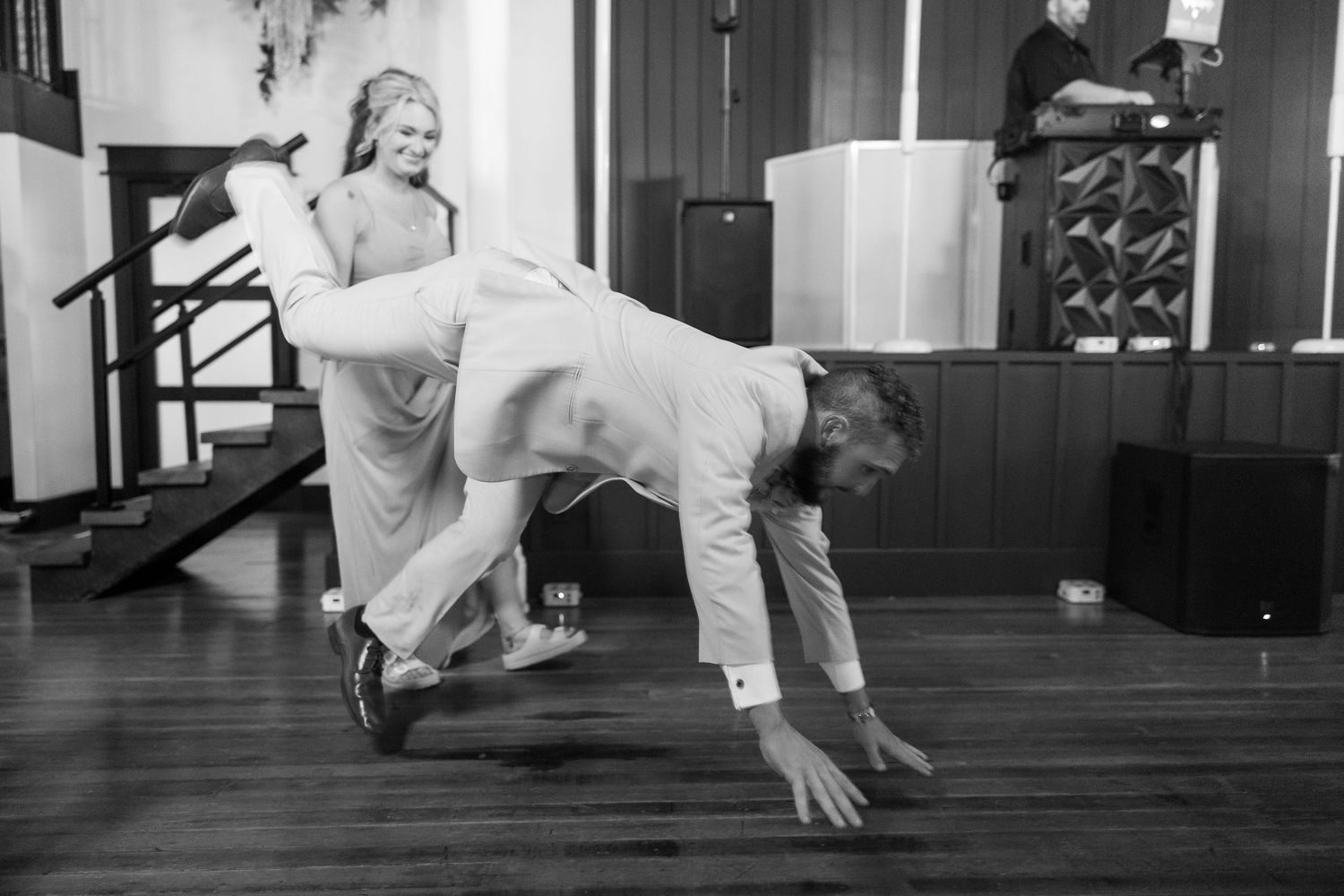 A playful black and white wedding photo showing a couple in a fun dance pose on a wooden floor.