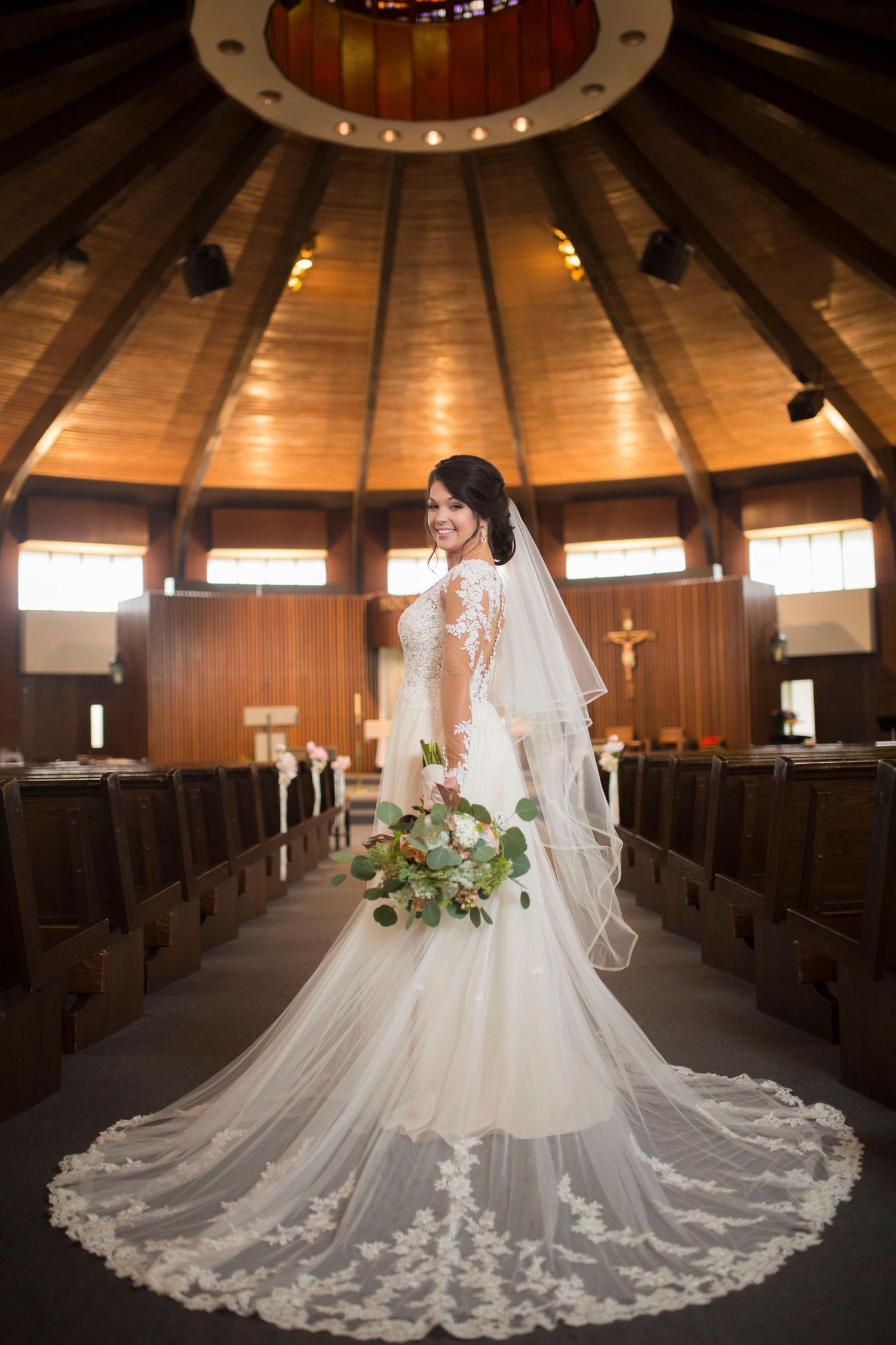 A stunning cathedral-style wedding dress with intricate lace details spreads across wooden church pews.