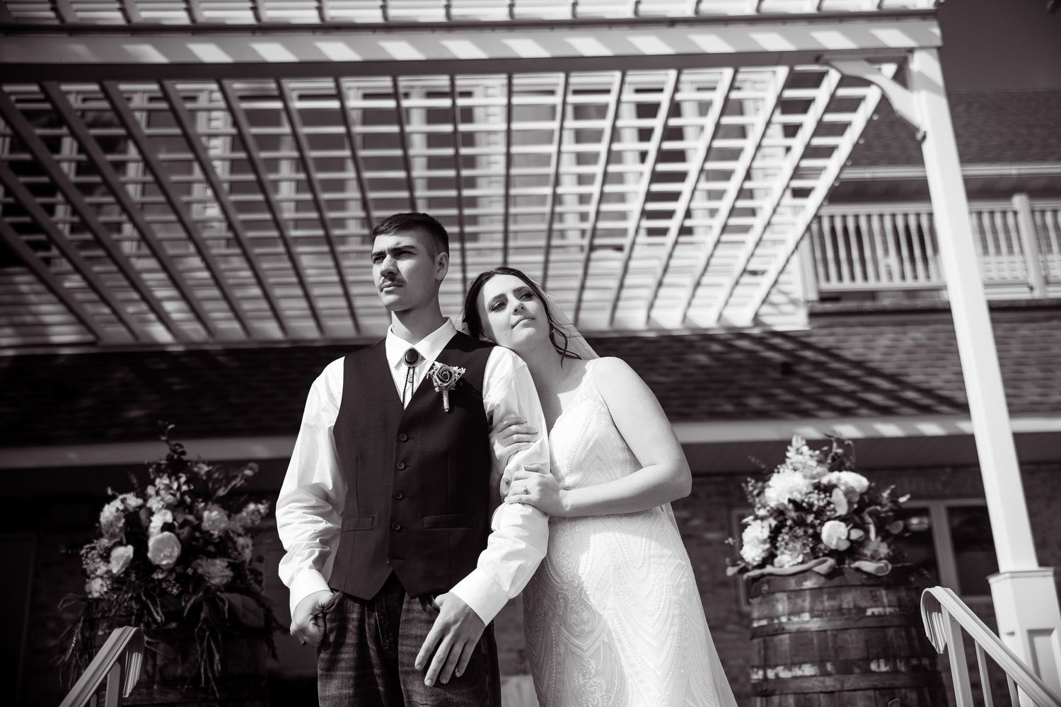 Bride and groom share a romantic moment under a pergola in black and white photo.