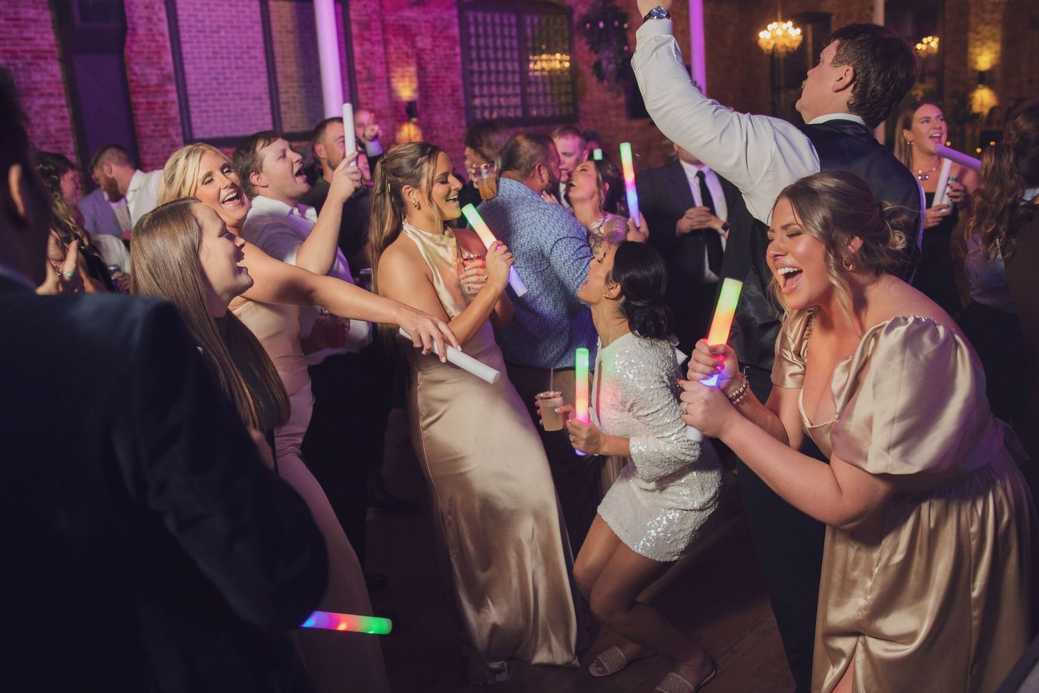 Wedding guests dancing and celebrating on colorfully lit dance floor.