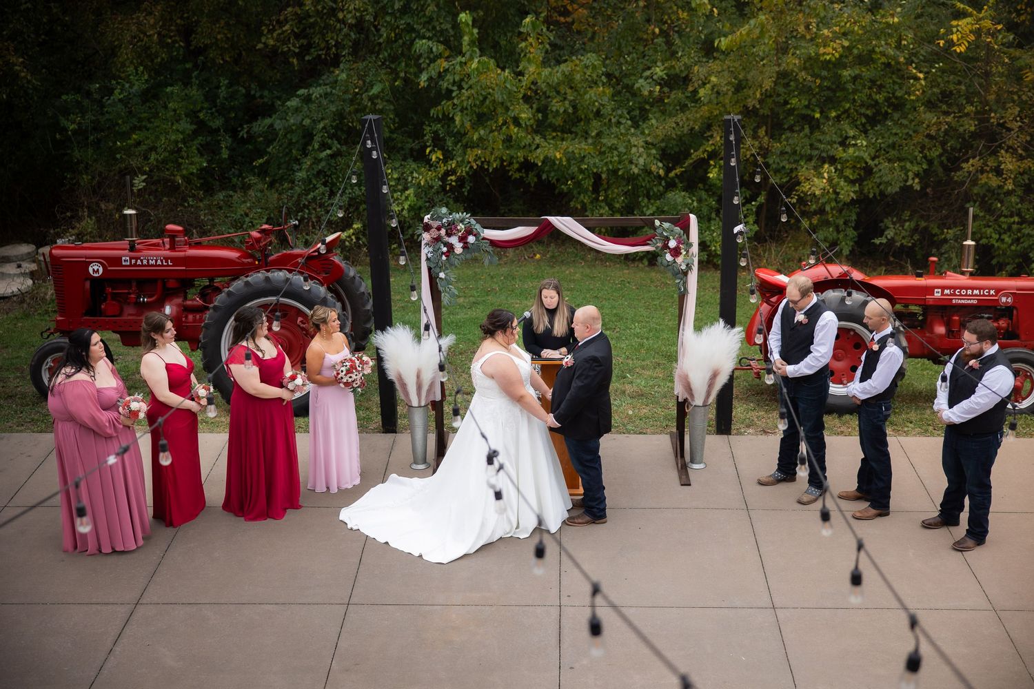 Wedding ceremony guests seated in white chairs on an outdoor patio with red floral decorations.