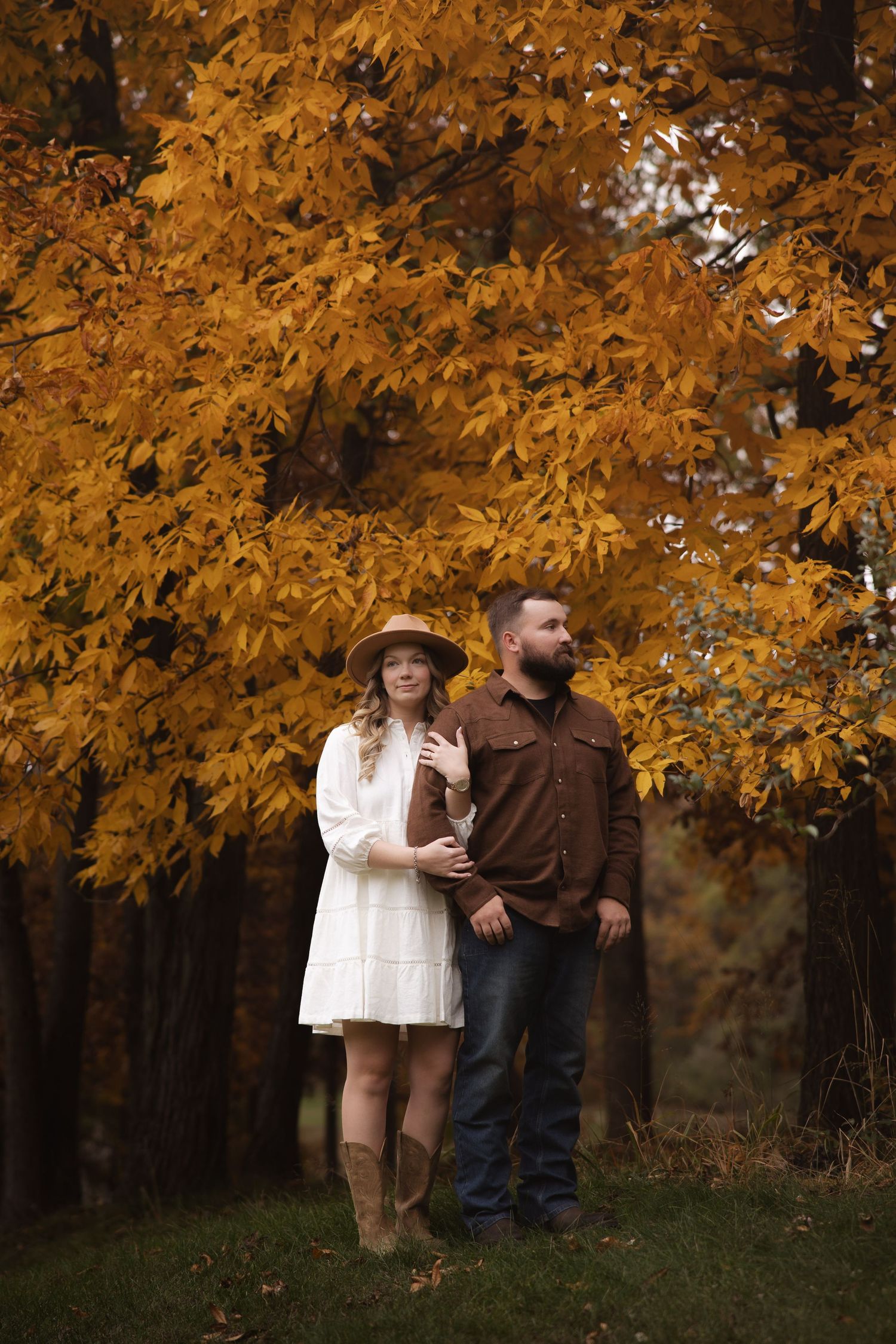 A couple stands together under vibrant orange autumn foliage in a romantic outdoor setting.