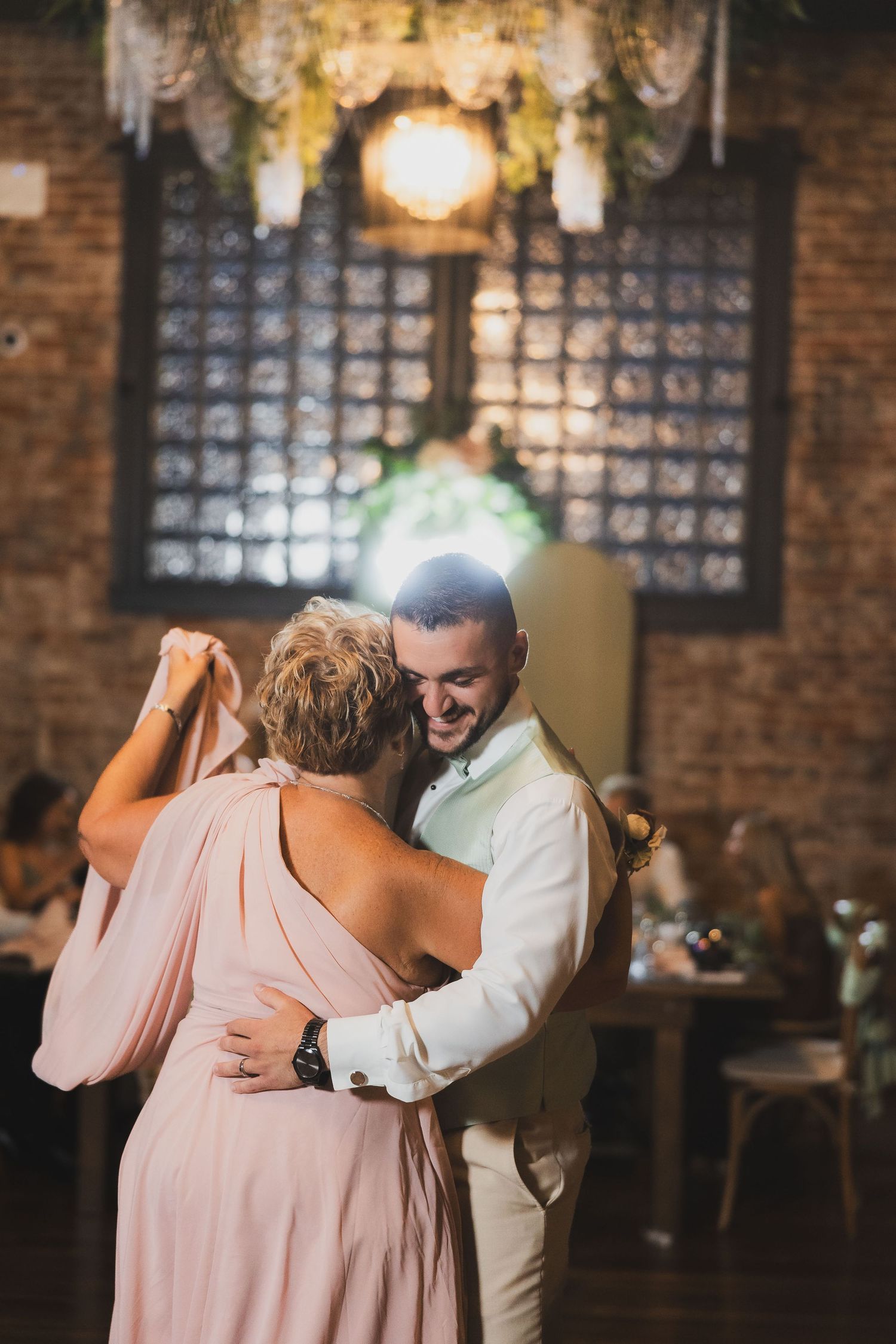 A couple shares an intimate dance moment in a rustic venue with exposed brick walls and warm lighting.